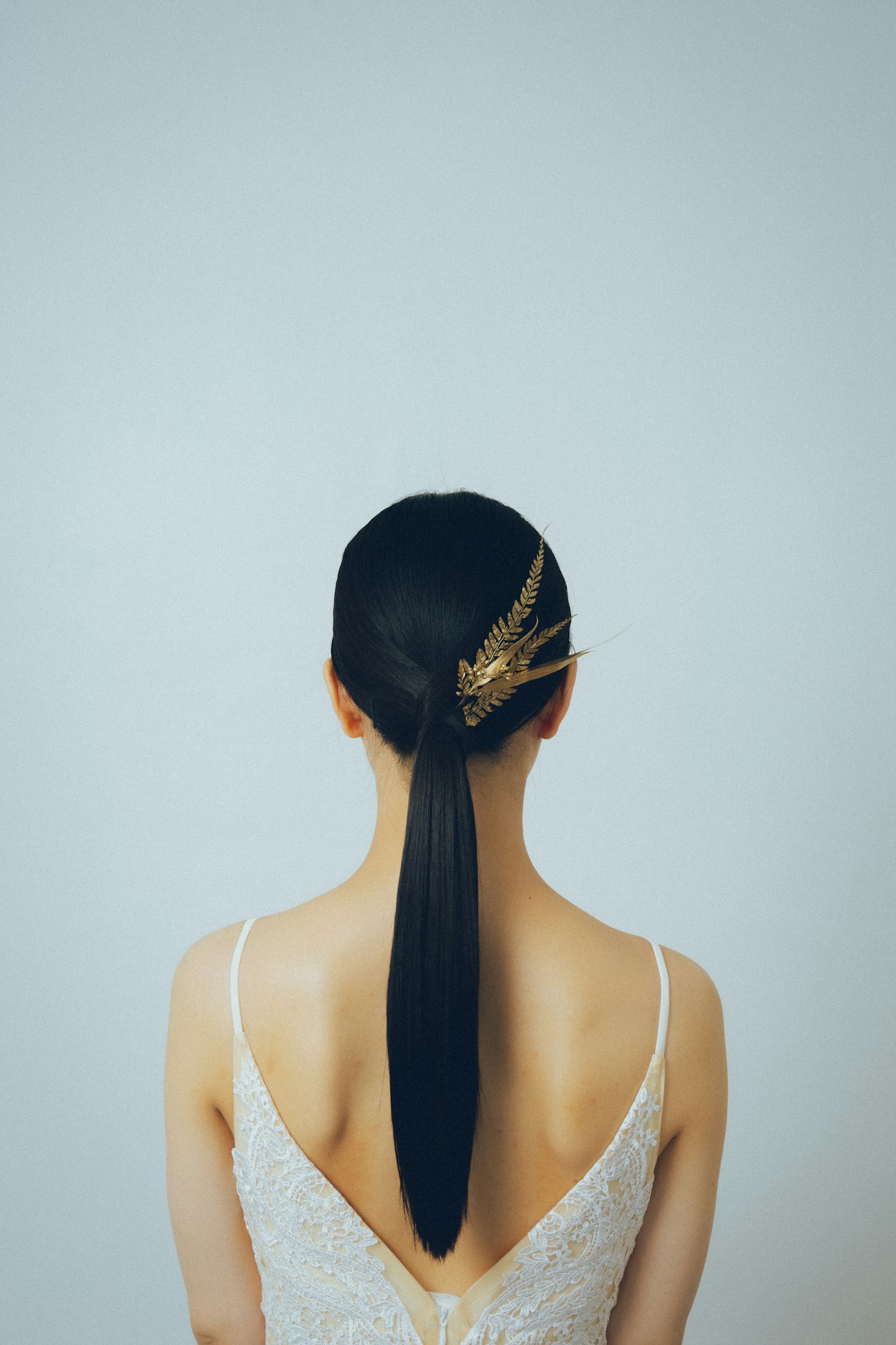 Vista da dietro di una donna con capelli neri lisci acconciati elegantemente e indossando un abito bianco