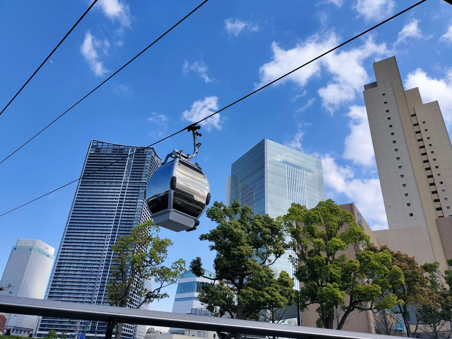 Un teleférico moviéndose a través de un paisaje urbano con rascacielos y un cielo azul