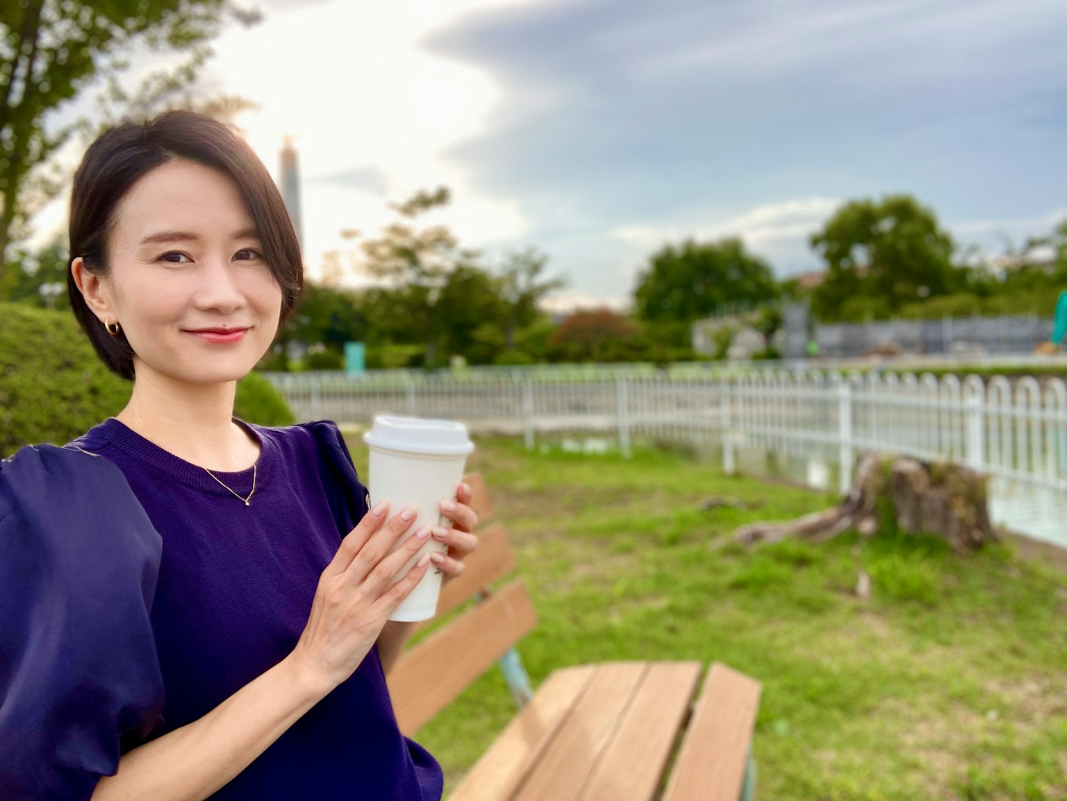 一位女性坐在公园长椅上，手里拿着咖啡杯，面带微笑