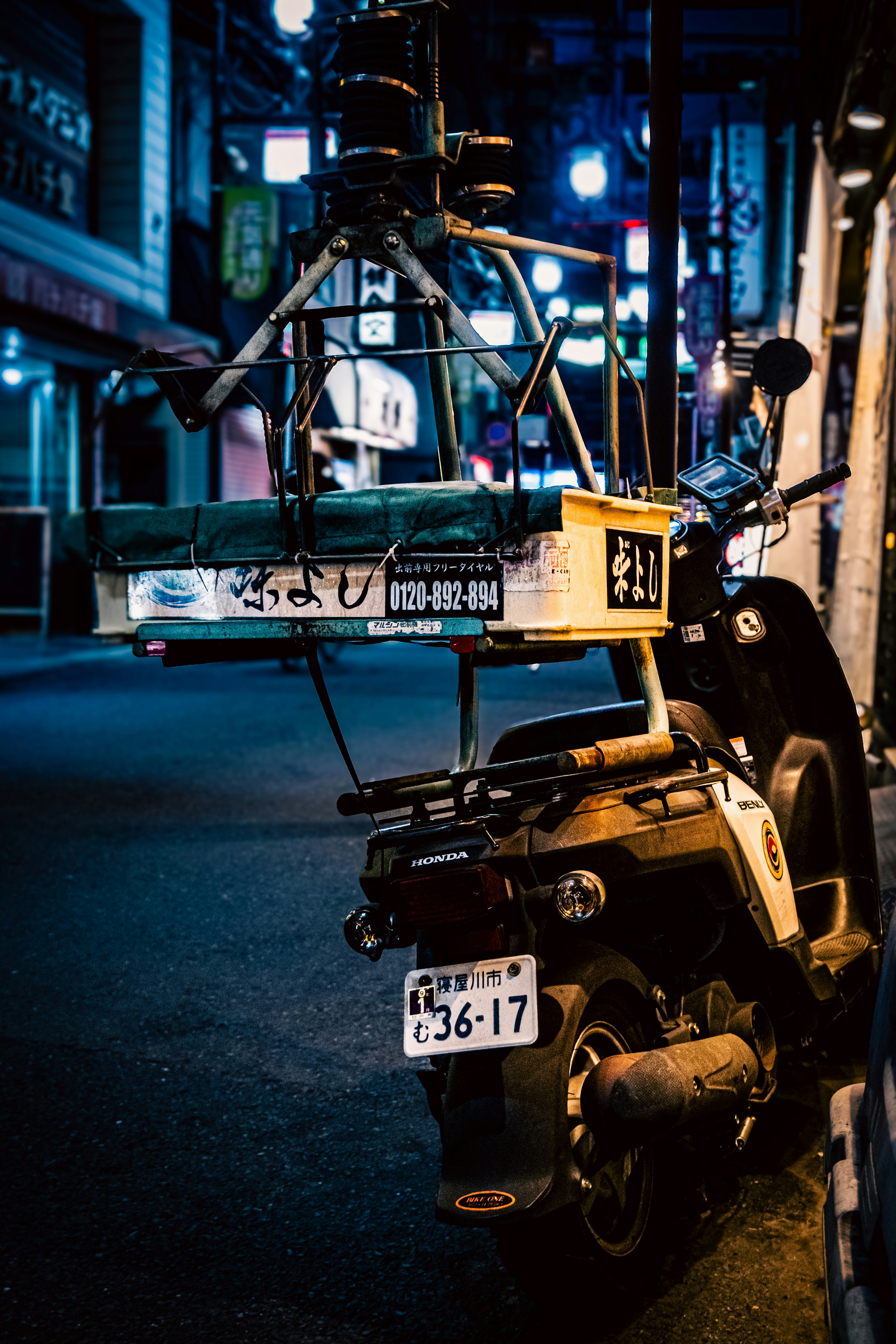 夜の路地に停まるバイクと街灯の光がにじむ風景