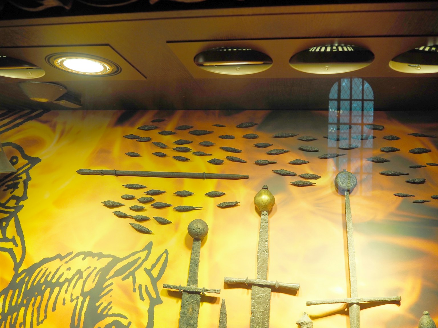 Immagine di spade e oggetti metallici esposti su un muro con uno sfondo colorato