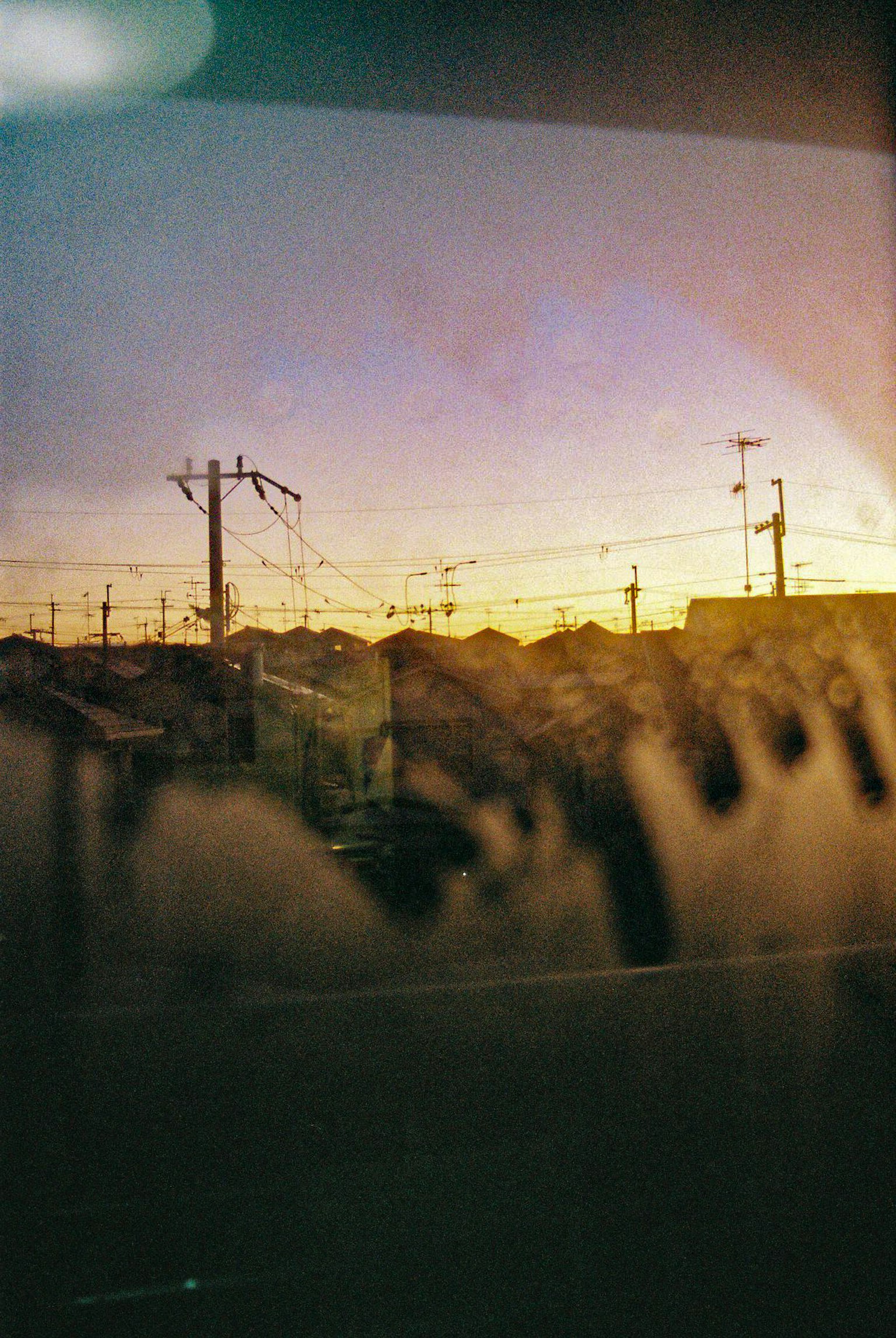Silhouette of utility poles against a sunset viewed through a car window