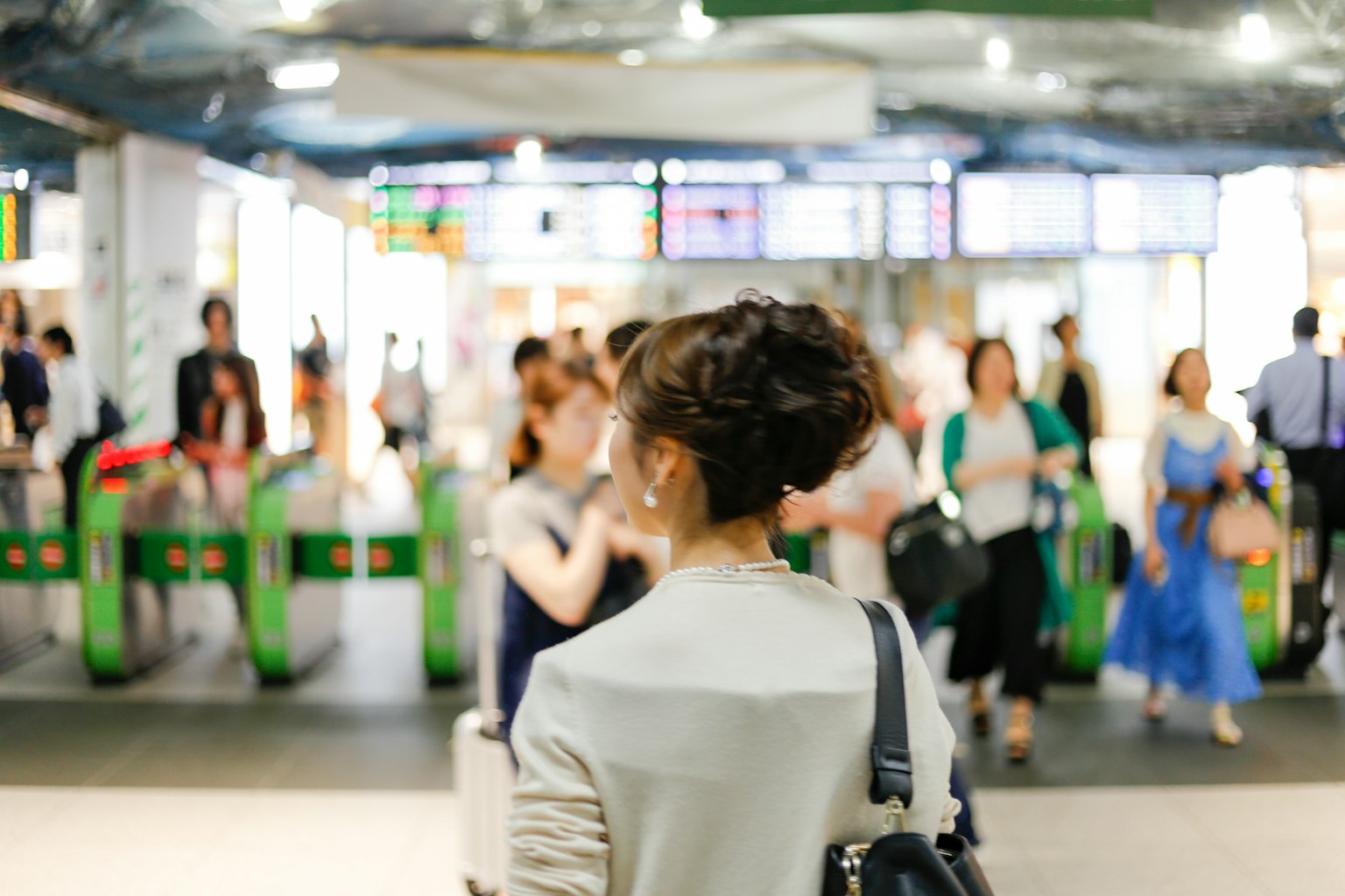 Frau von hinten in einem belebten Bahnhof mit Drehkreuzen und Reisenden