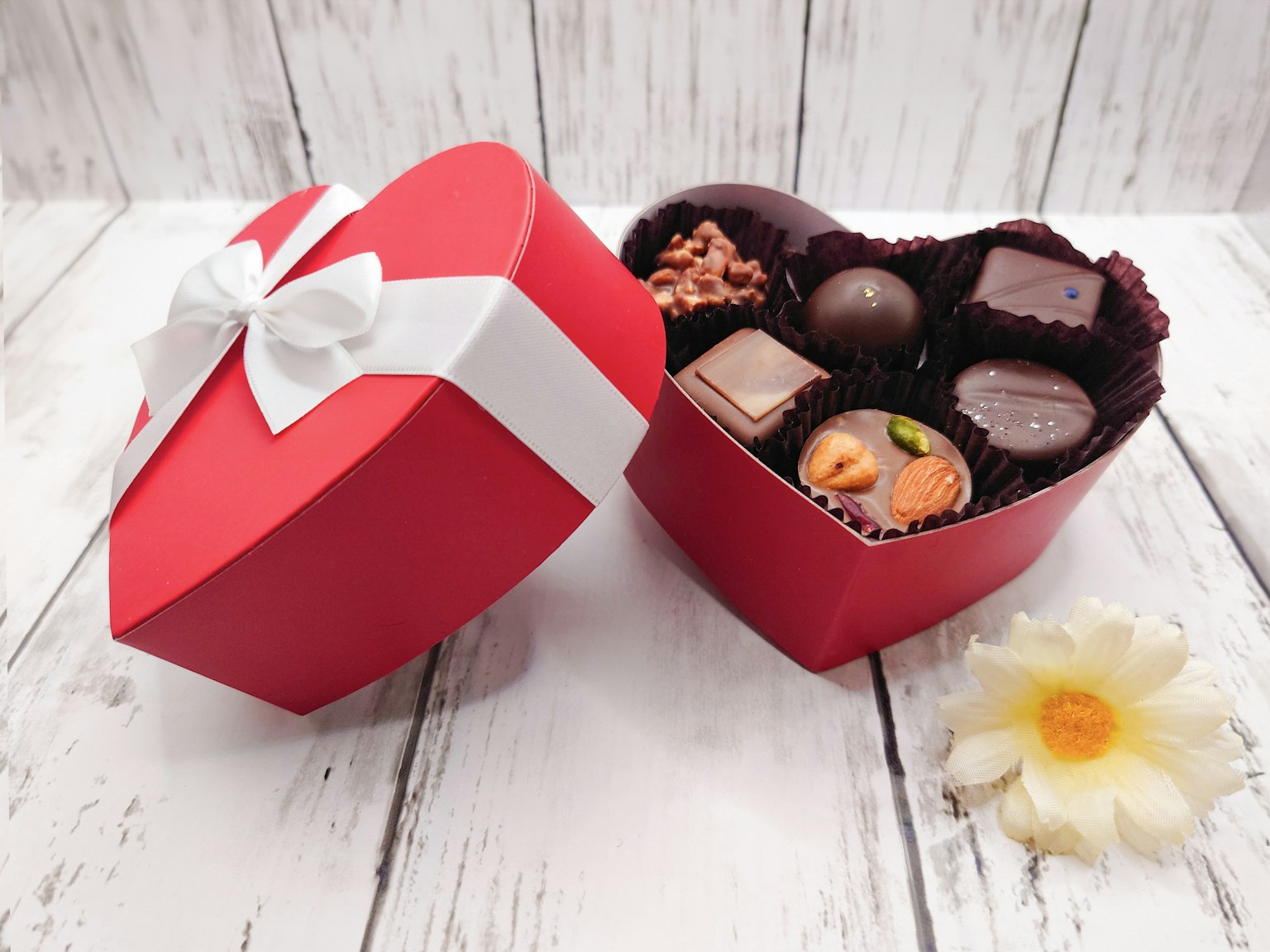 Scatola a forma di cuore rosso piena di cioccolatini assortiti e un fiore