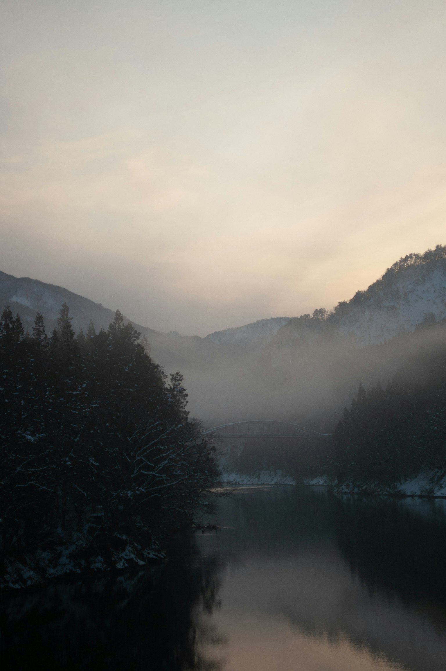 Paesaggio montano sereno con un fiume nebbioso e una dolce luce serale