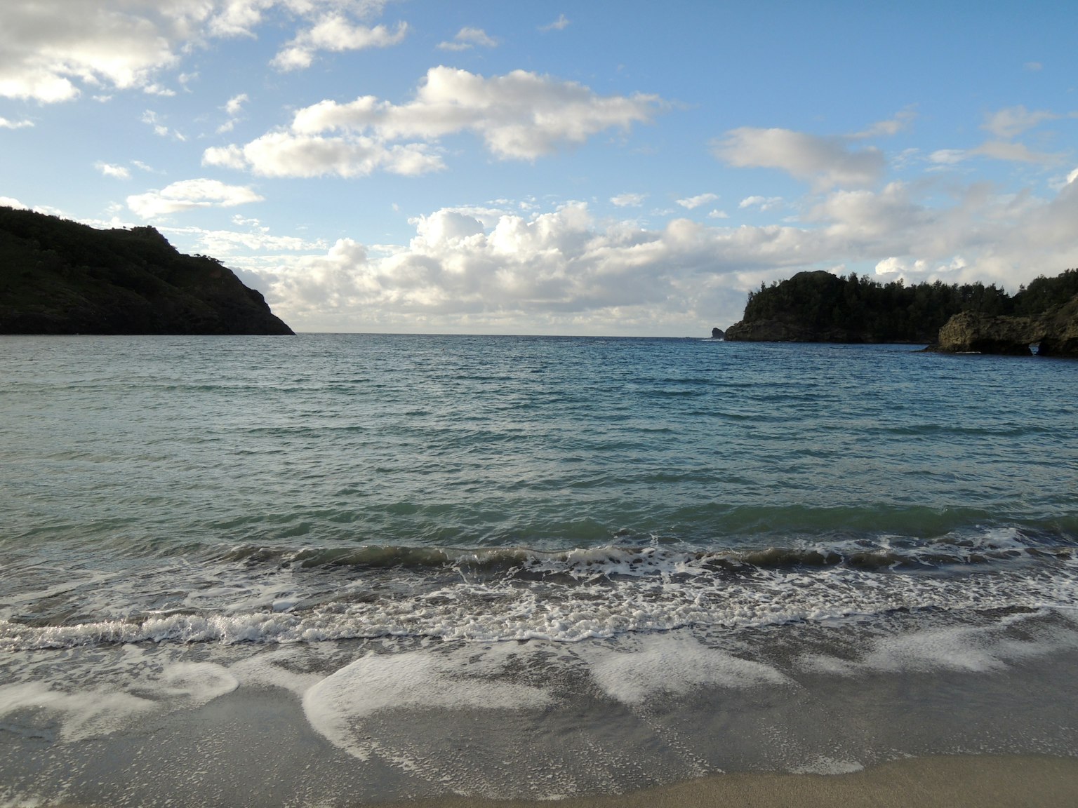 Scenic view of blue ocean and white sandy beach with rolling clouds and hills