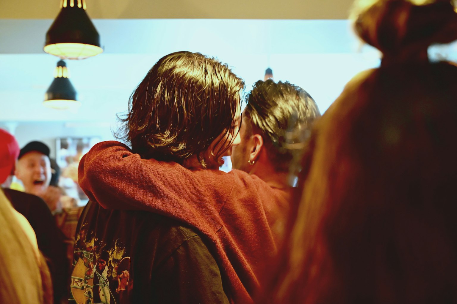 Two people embracing in a casual setting with others in the background