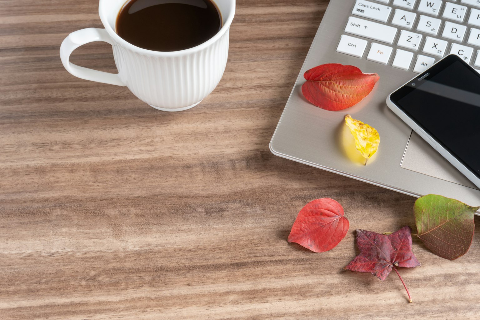 Sebuah adegan meja dengan cangkir kopi dan keyboard, kelopak bunga berwarna-warni berserakan