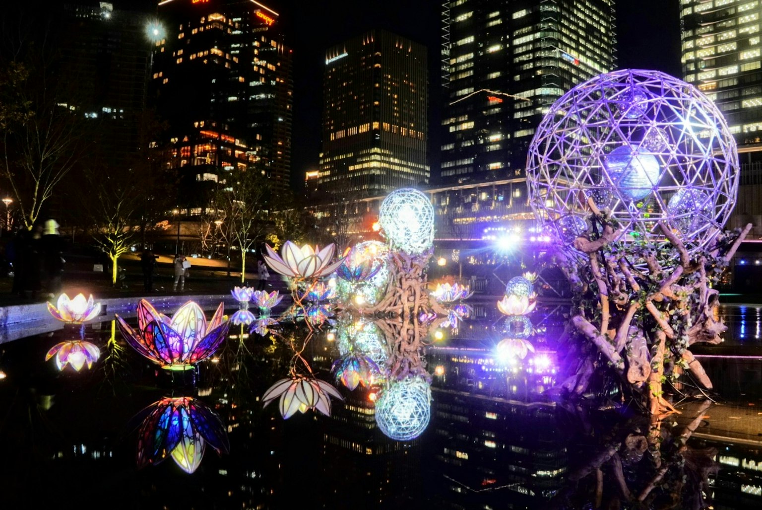 Fleurs et objets colorés illuminés se reflétant sur l'eau avec une skyline urbaine la nuit