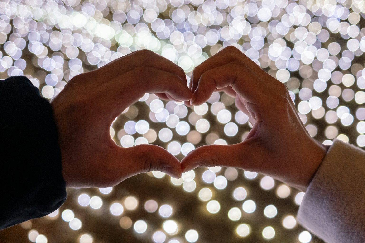 Dos manos formando un corazón contra un fondo de luces borrosas