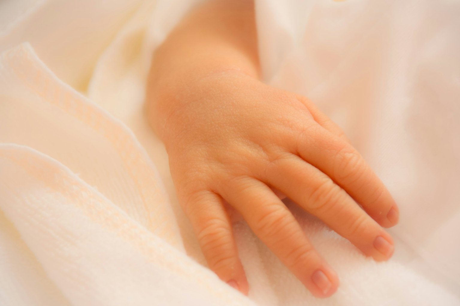 Una mano de bebé descansando sobre una suave tela blanca