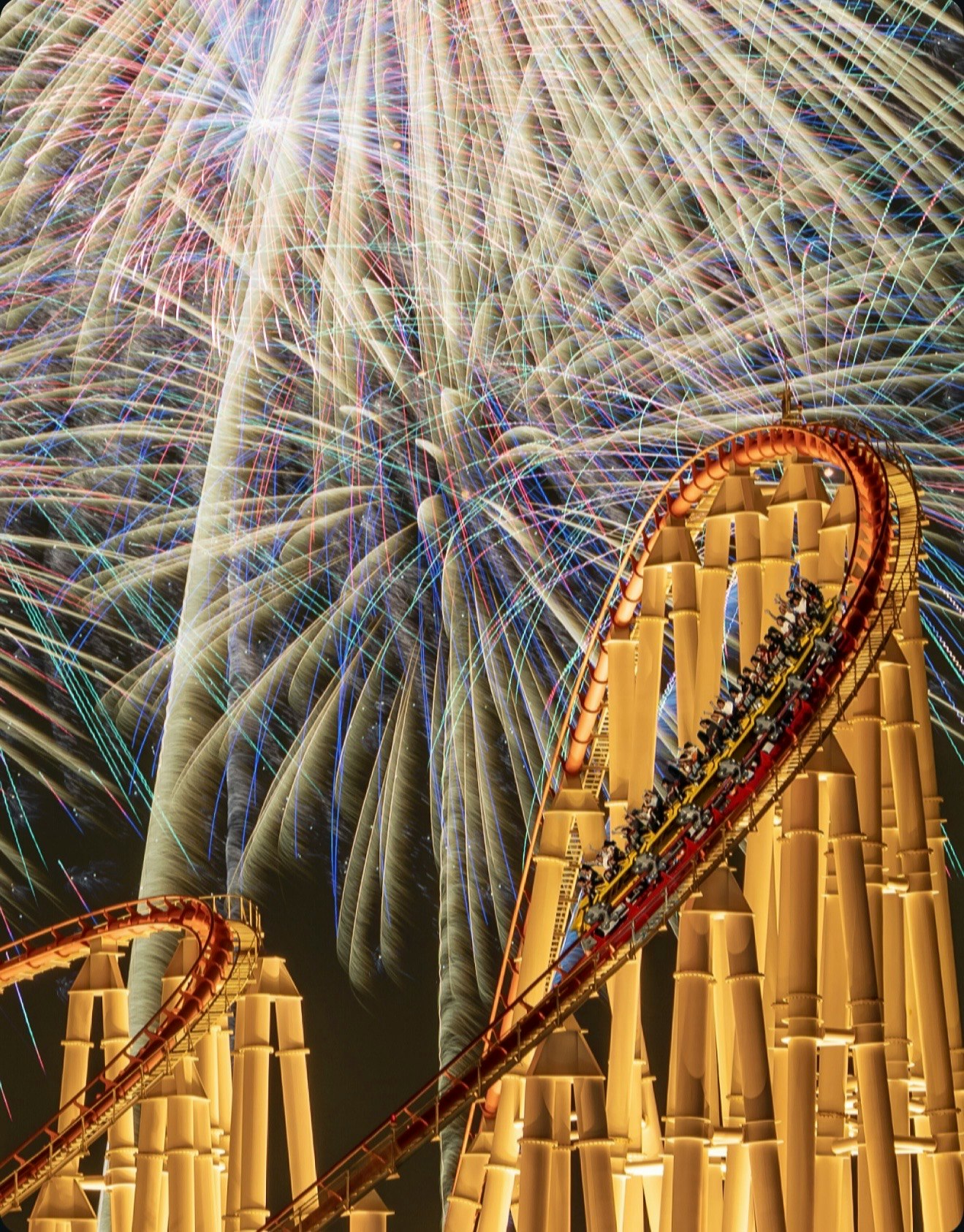 scena notturna con effetti luminosi simili a fuochi d’artificio e un roller coaster