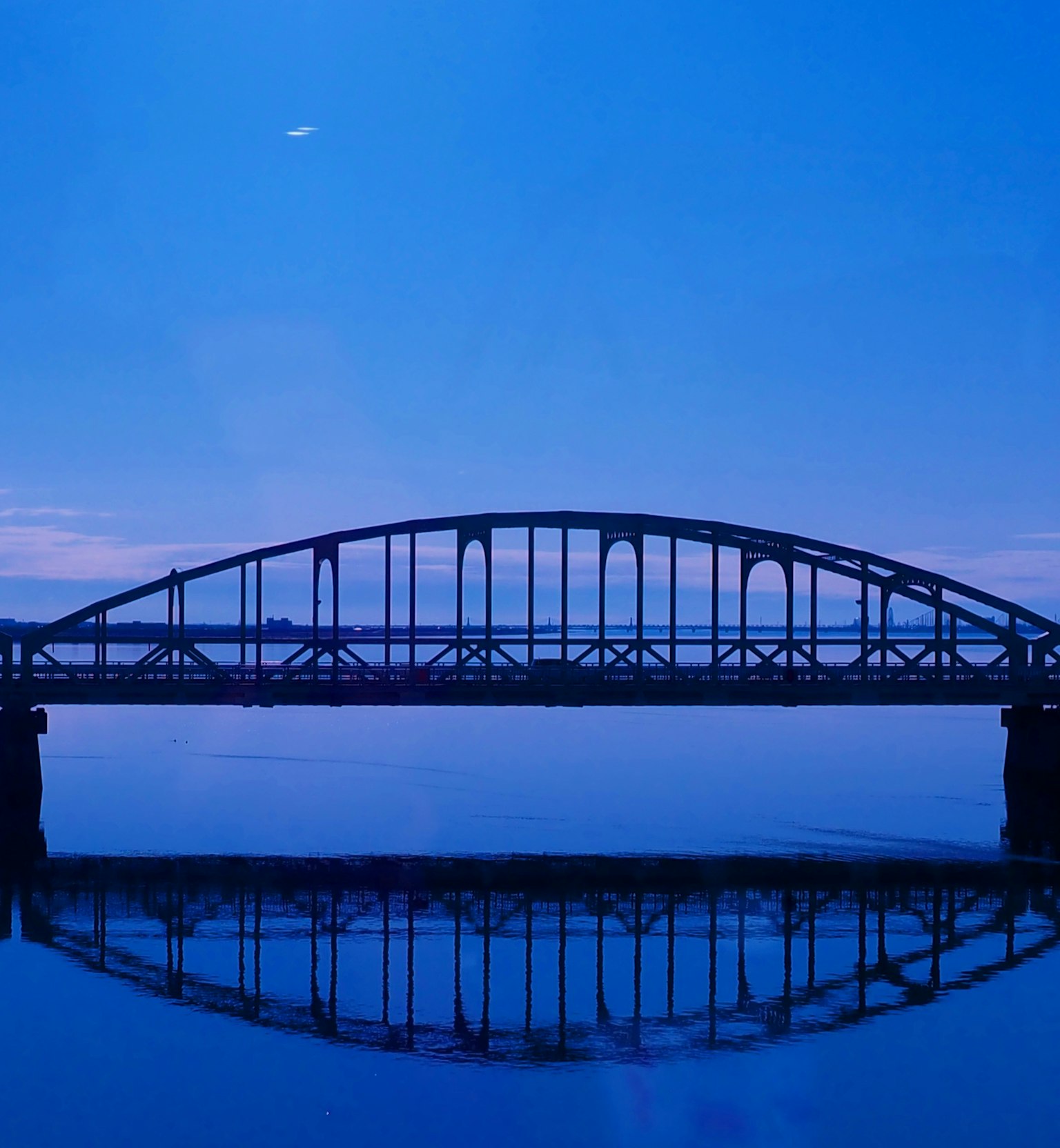Silueta de un puente bajo un cielo azul con reflejo en el agua