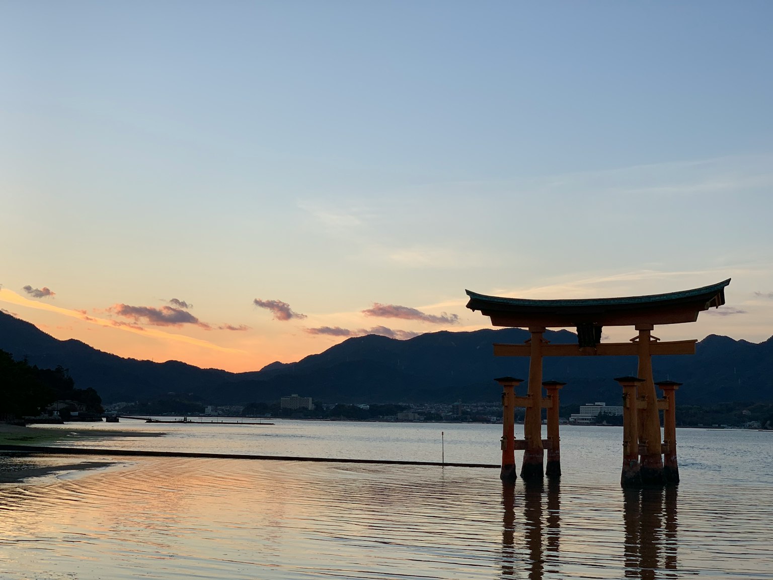 Torii gate silhouetted against a sunset over calm waters and mountains