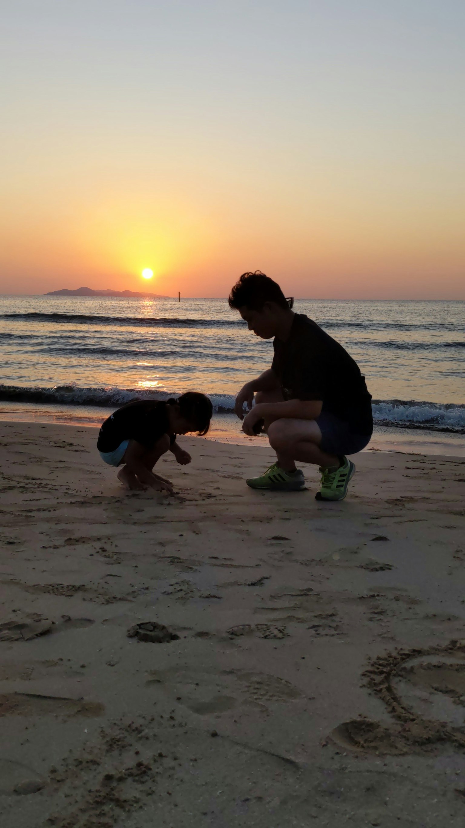 日落時在海灘上玩耍的父母和孩子的剪影