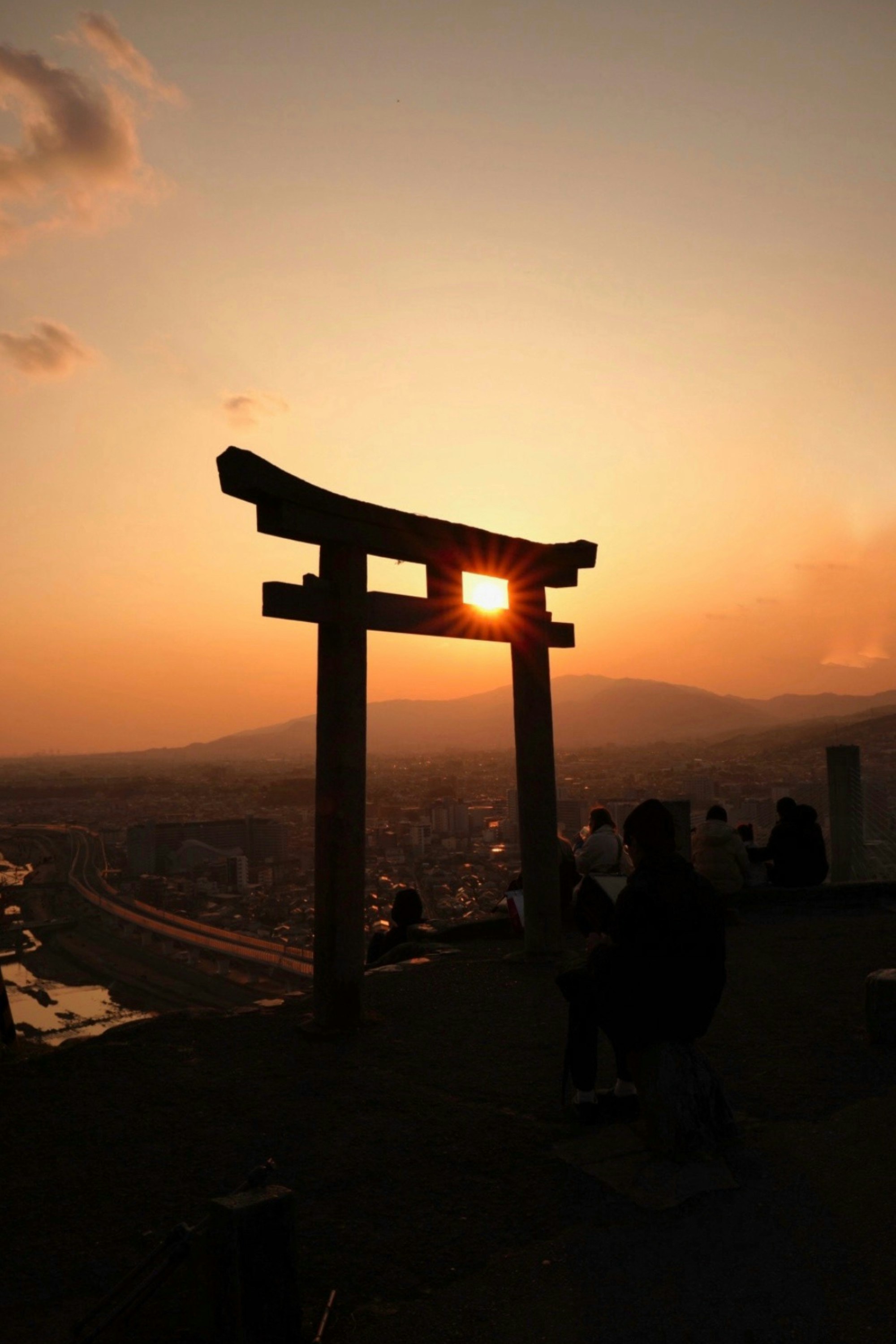 夕日を背景に鳥居のシルエットと人影が並ぶ展望スポット