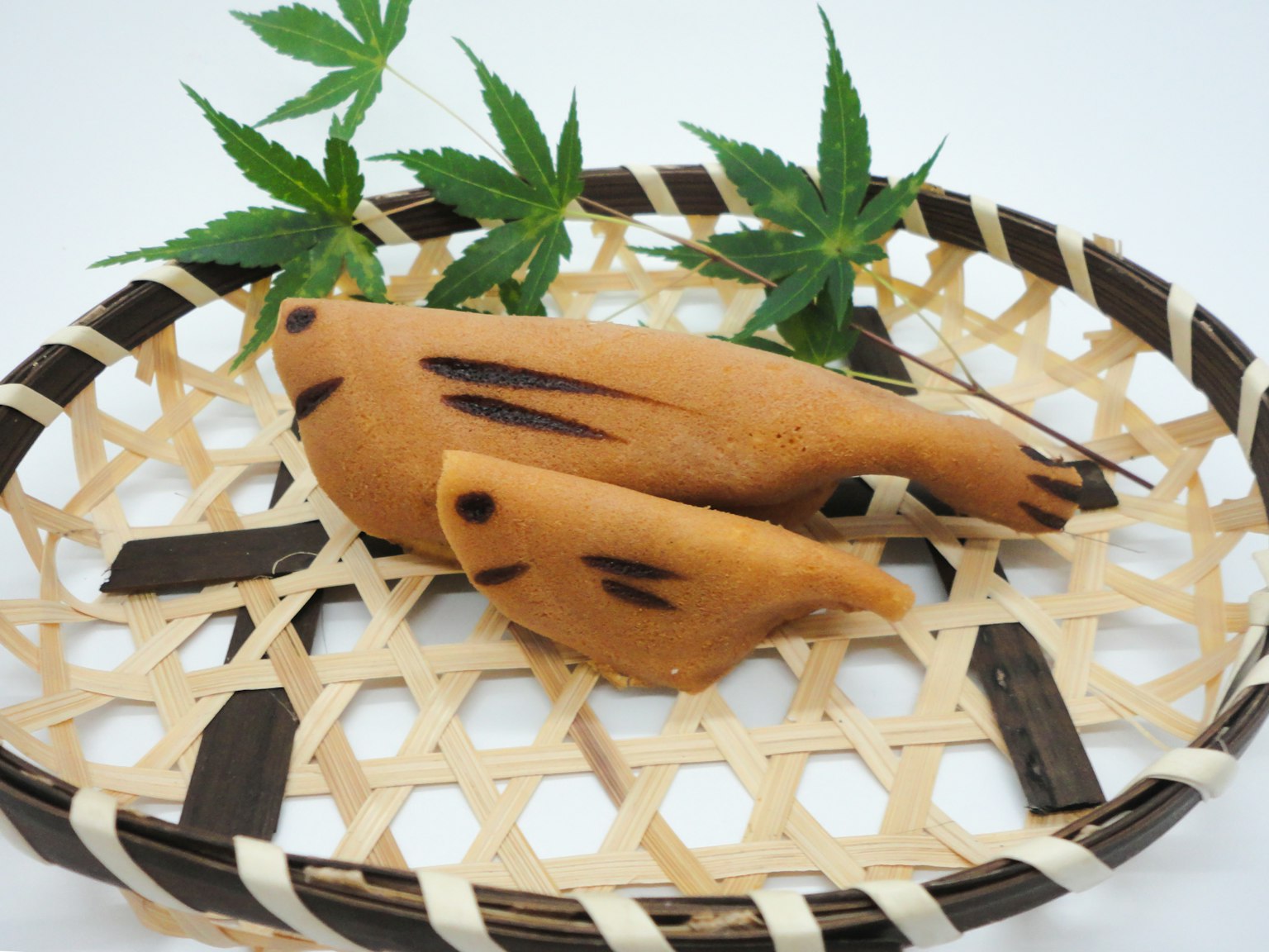 Due wagashi a forma di pesce su un cesto di bambù con foglie verdi