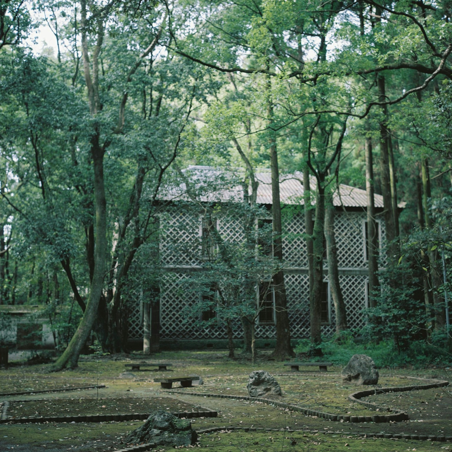 An old lattice-style building nestled in a lush green forest with a stone garden