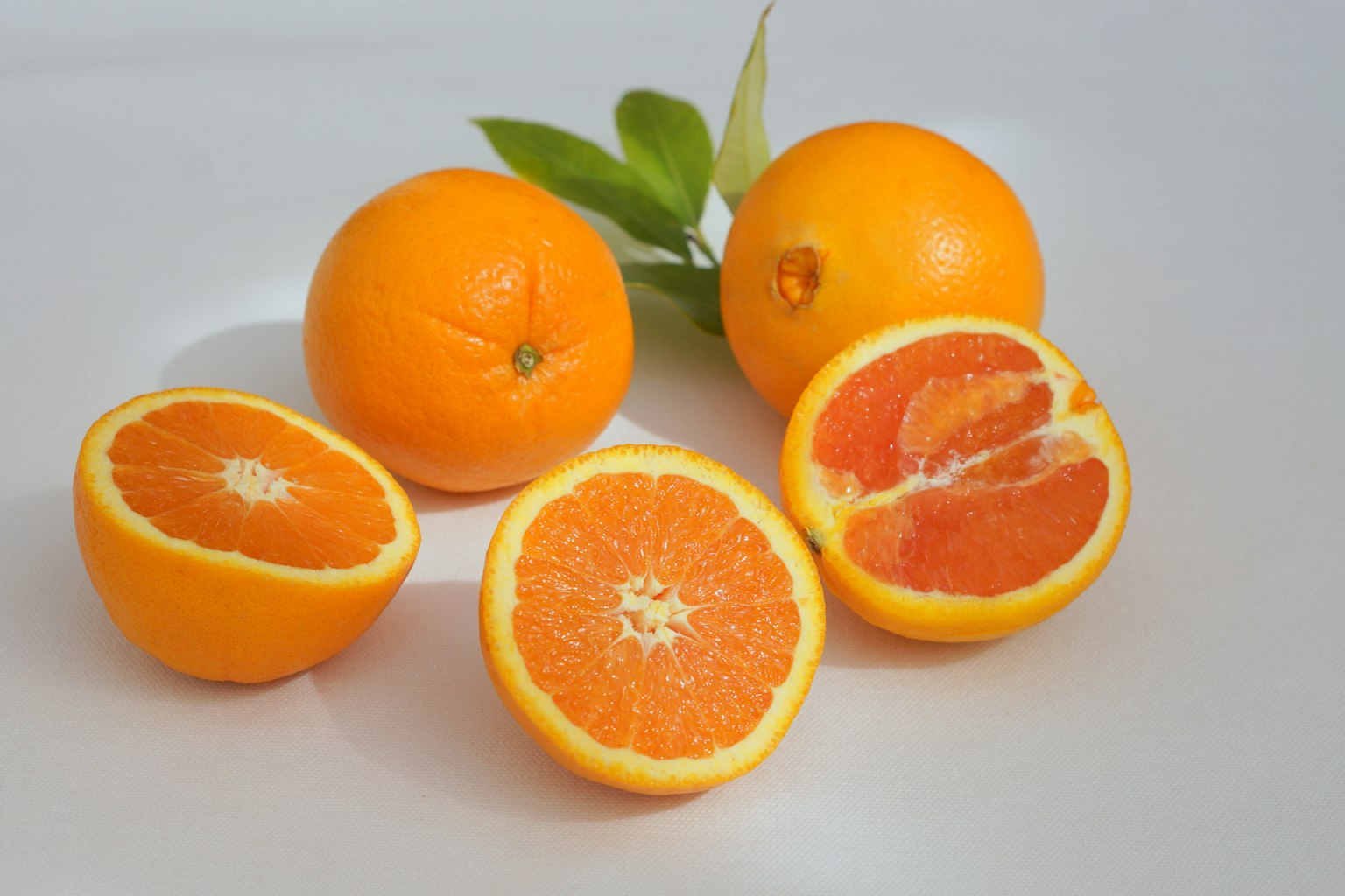Imagen de naranjas con una cortada a la mitad mostrando el interior jugoso y hojas verdes