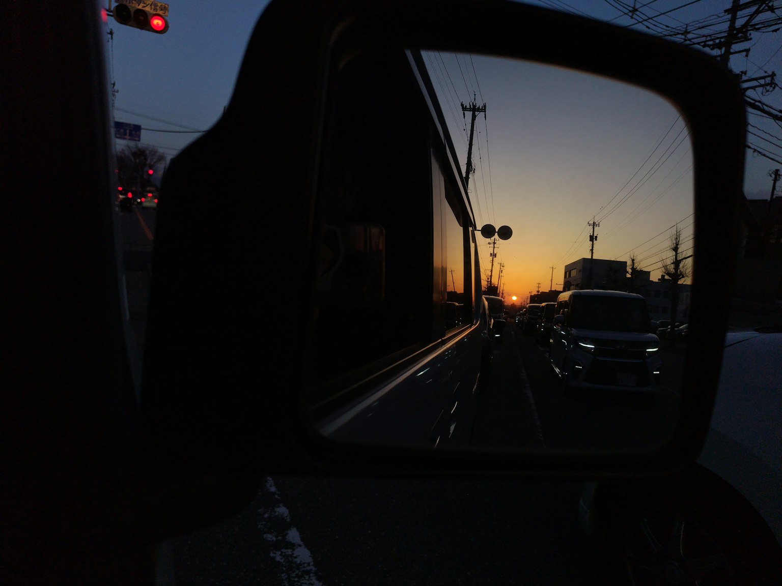 夕陽下汽車側鏡中反射的城市景觀和車輛輪廓