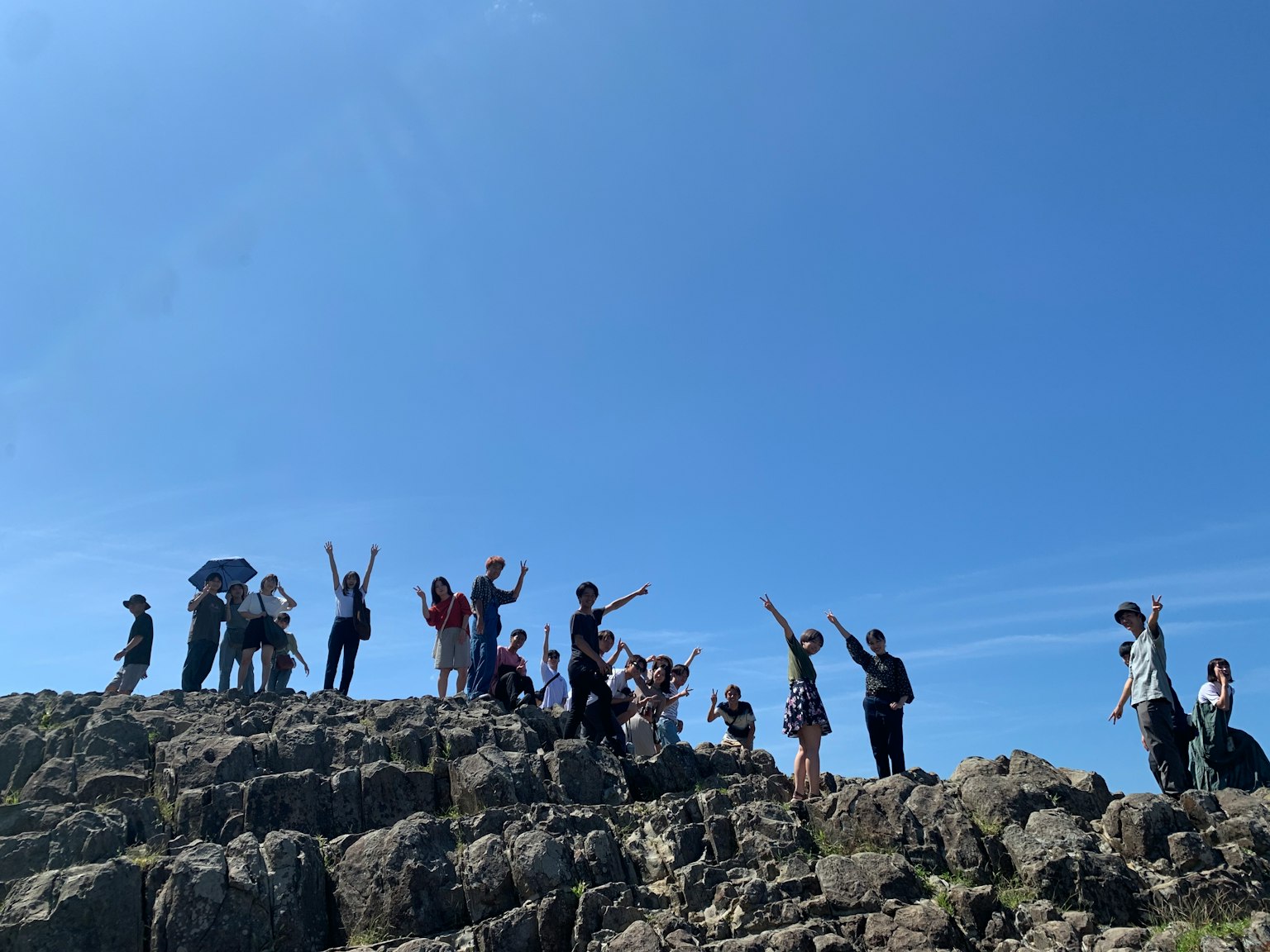 Group of people waving on rocky terrain under a clear blue sky