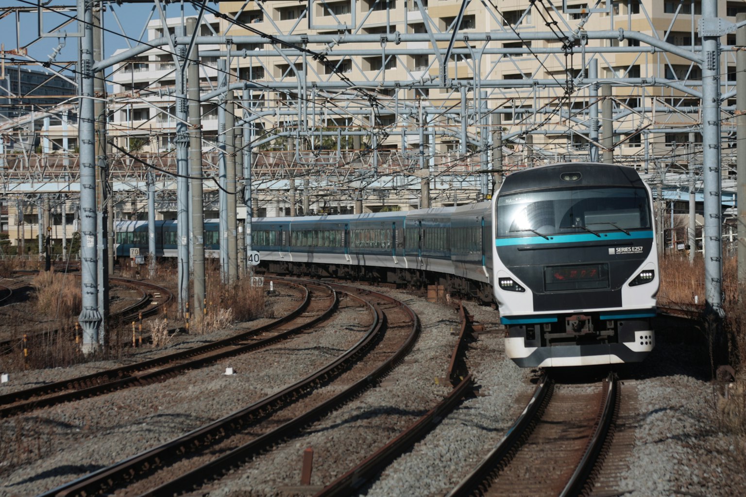 Un treno che percorre una curva con linee elettriche e edifici sullo sfondo