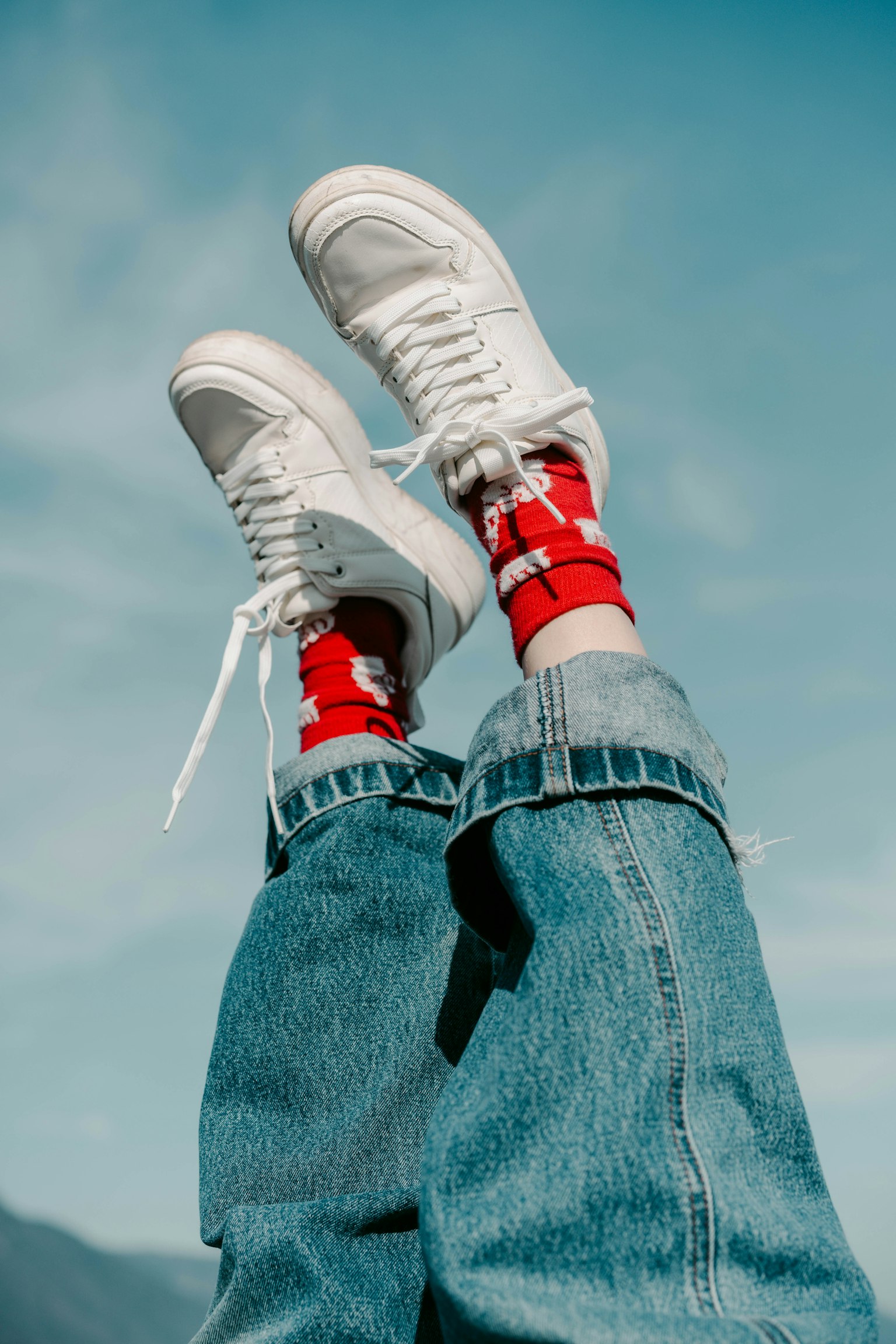 Füße in weißen Sneakers und roten Socken vor blauem Himmel