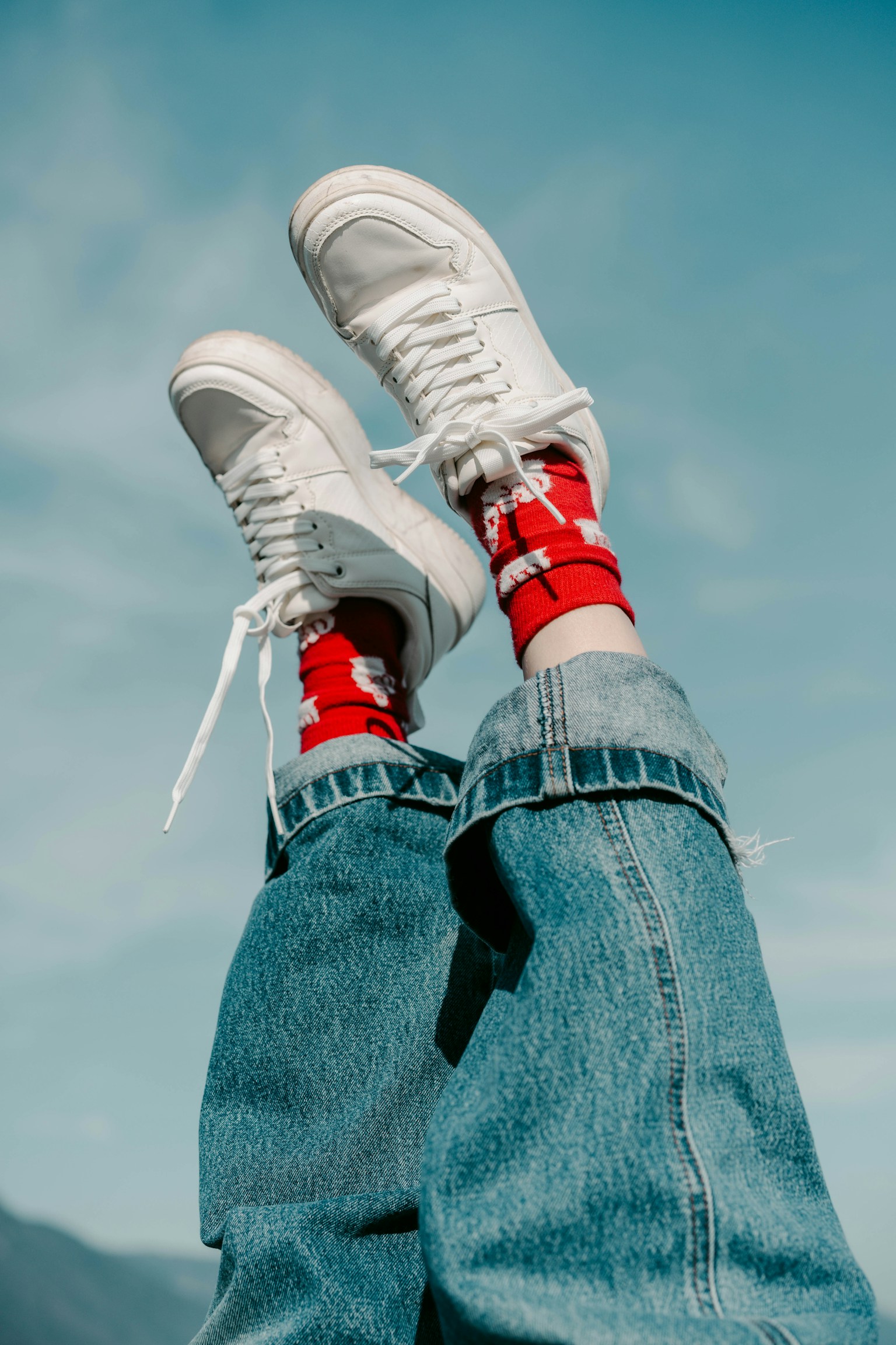 Pieds portant des baskets blanches et des chaussettes rouges sur fond de ciel bleu