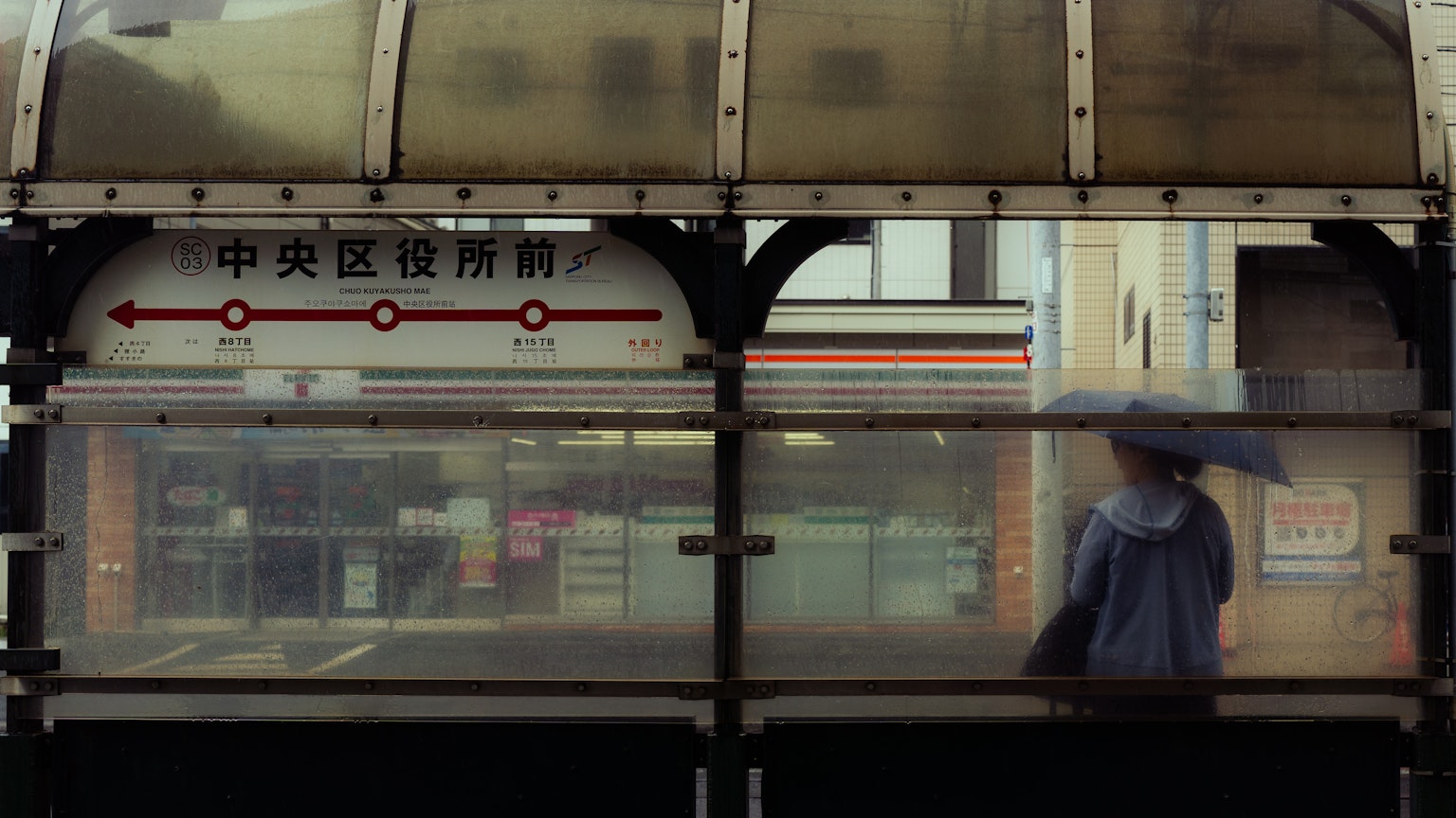 A bus stop scene with a person holding an umbrella in the rain