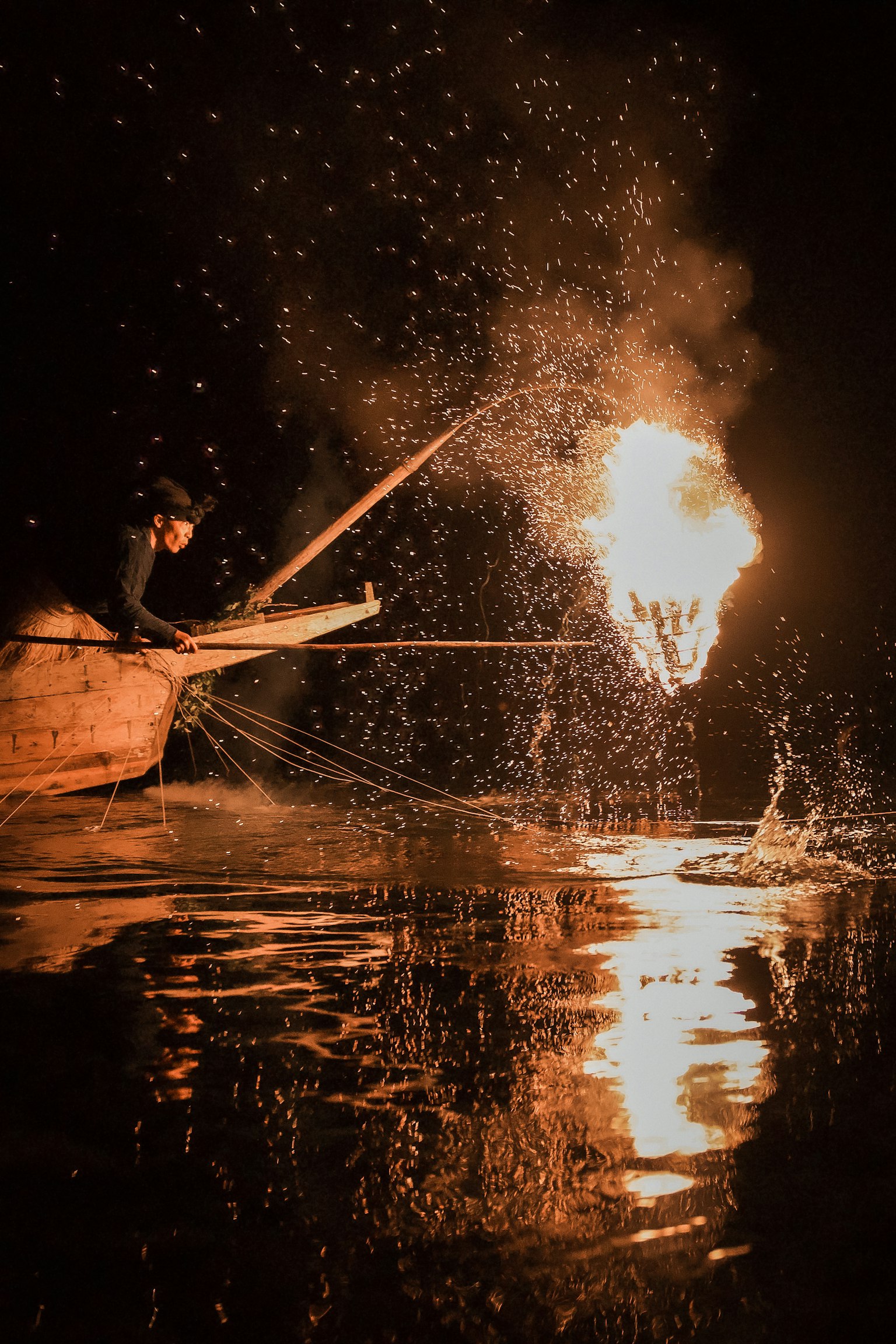 Pescador usando fuego para atrapar peces en una superficie de agua oscura