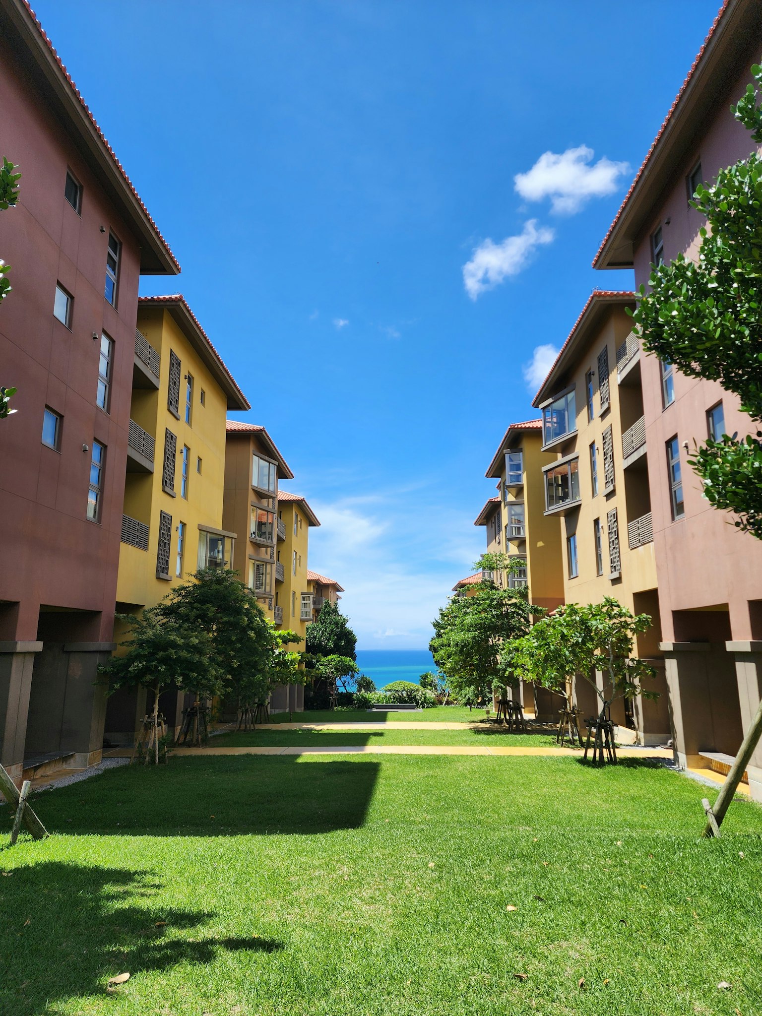 Bangunan apartemen berwarna-warni dikelilingi oleh rumput hijau dan pohon-pohon dengan pemandangan laut biru