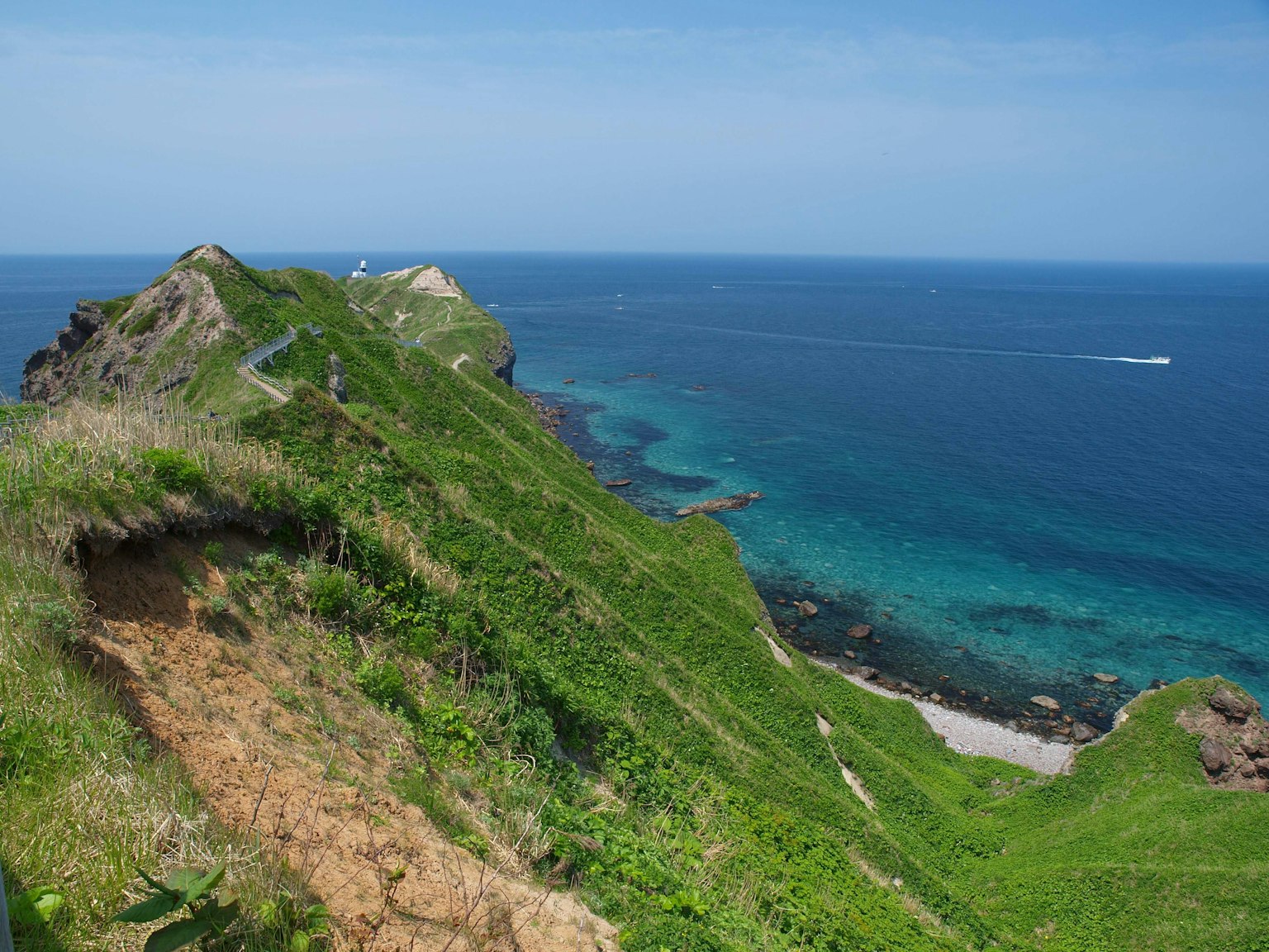 綠色山丘和藍色海洋的風景 遠處有一艘船