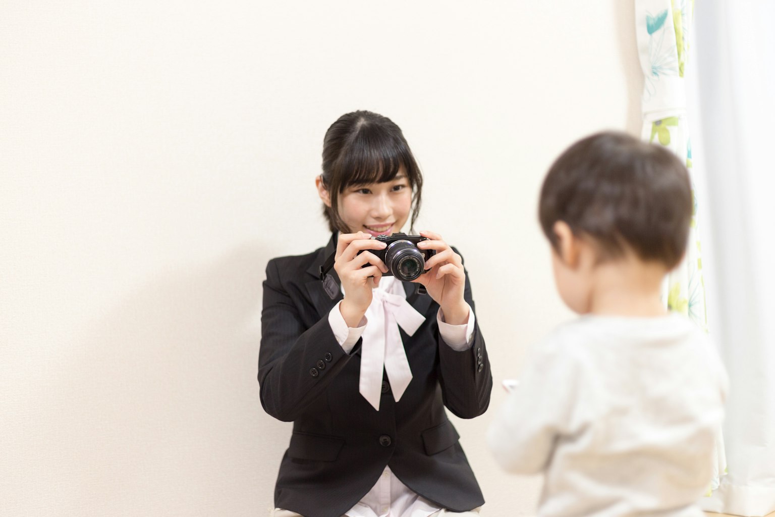 A woman in a suit holding a camera facing a child