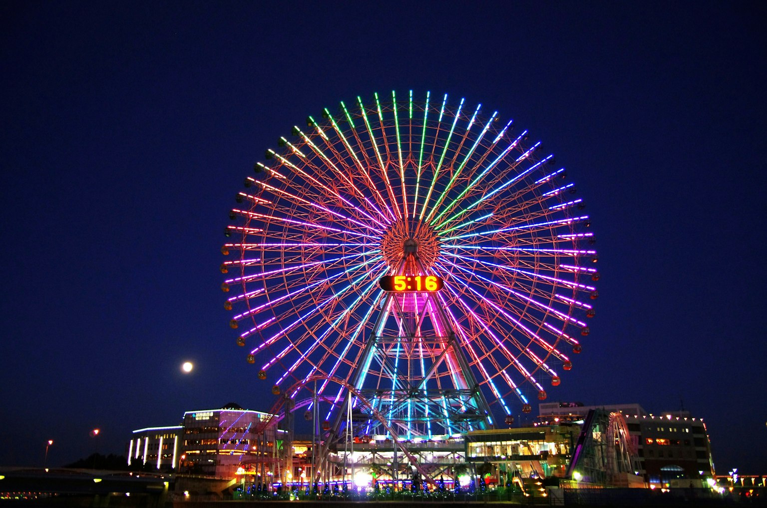 Grande roue colorée illuminée la nuit avec des bâtiments environnants