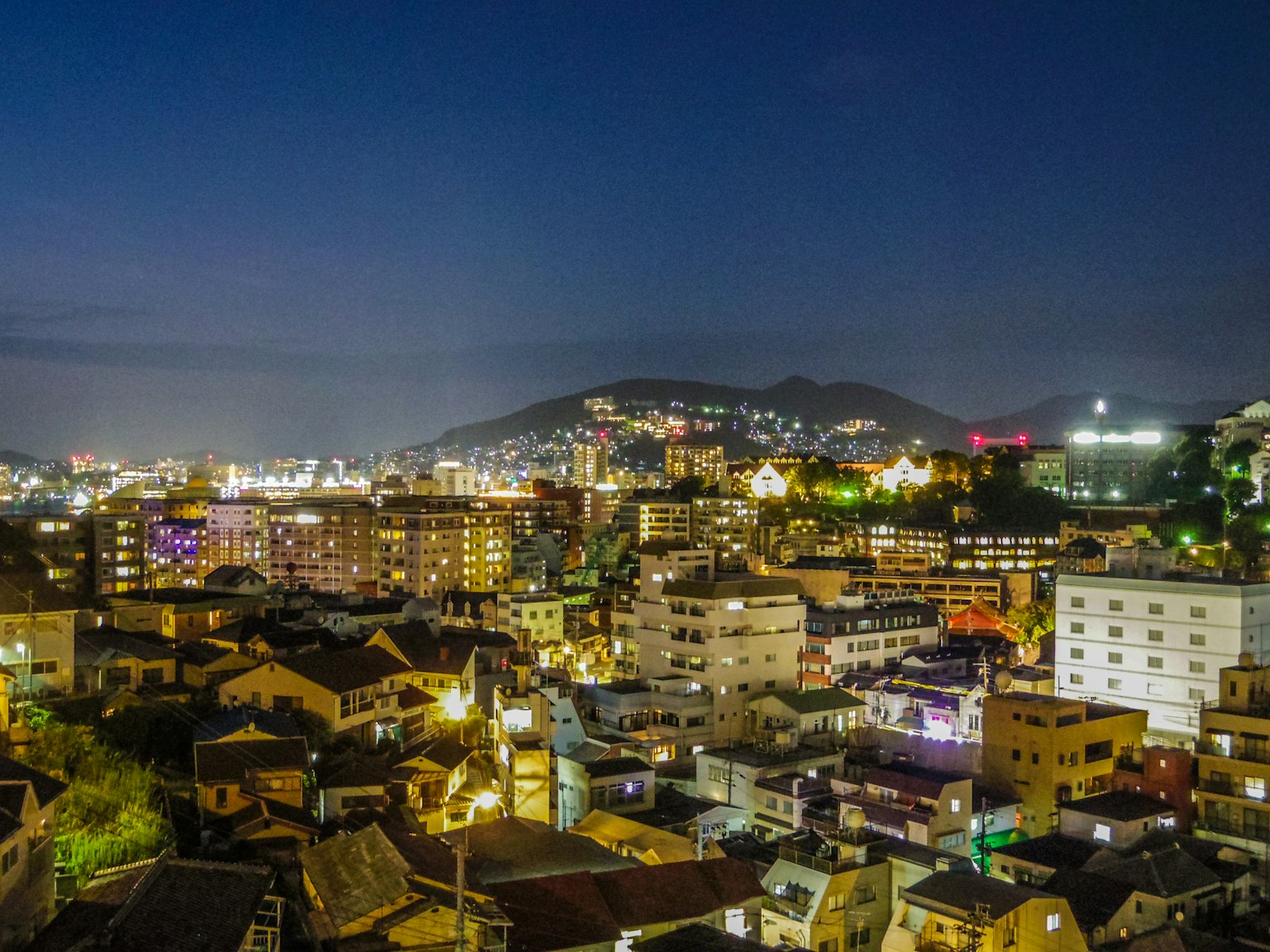 Night cityscape with illuminated buildings and mountain silhouette