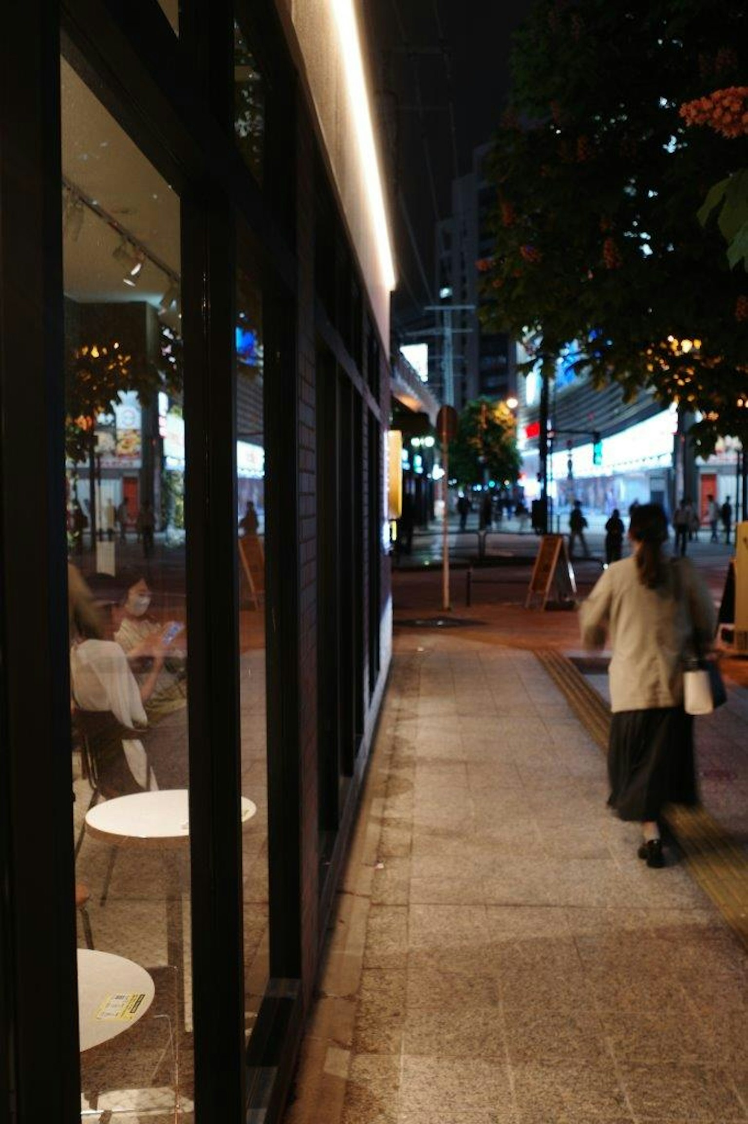 Nighttime urban scene featuring a cafe exterior illuminated by lights with pedestrians walking
