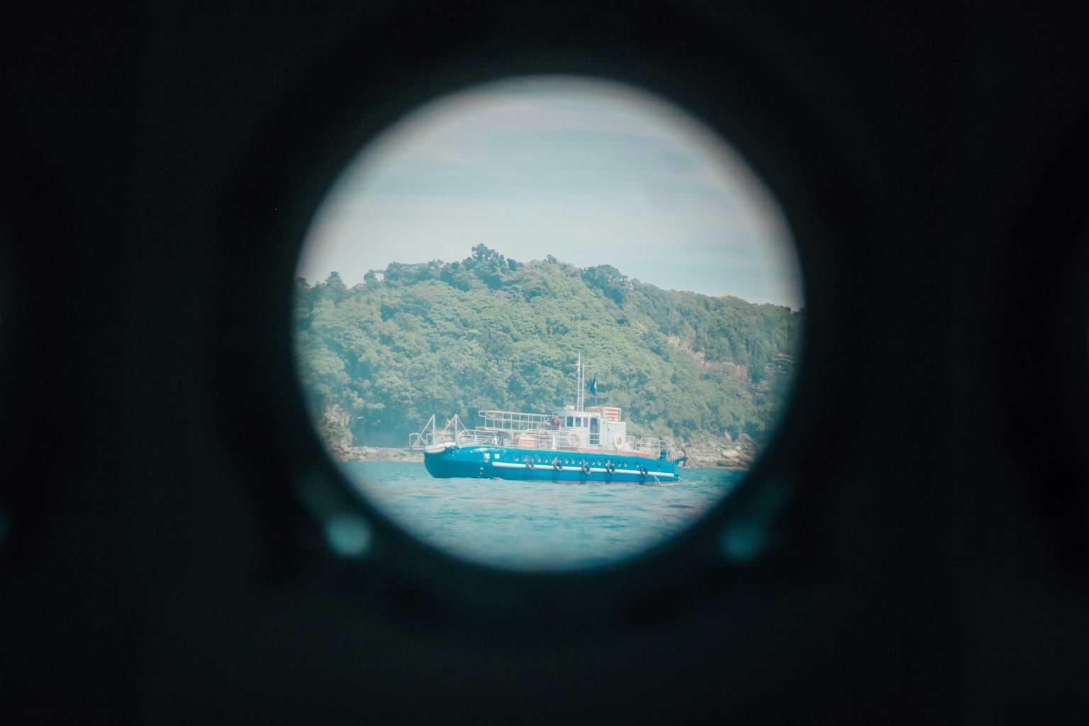 Eine Aussicht auf ein blaues Schiff auf dem Wasser durch ein rundes Fenster