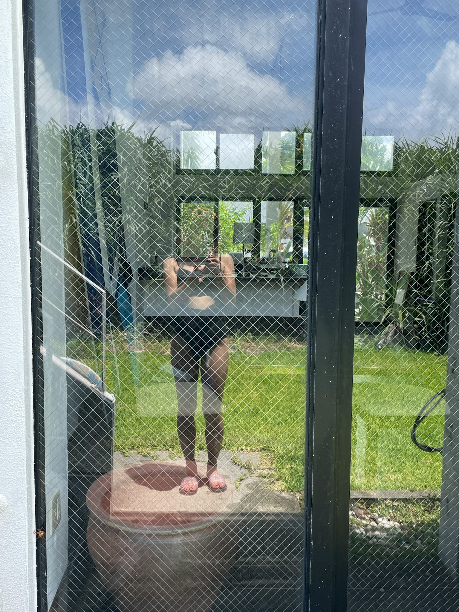 Person reflected in a glass door with a mesh design overlooking a garden
