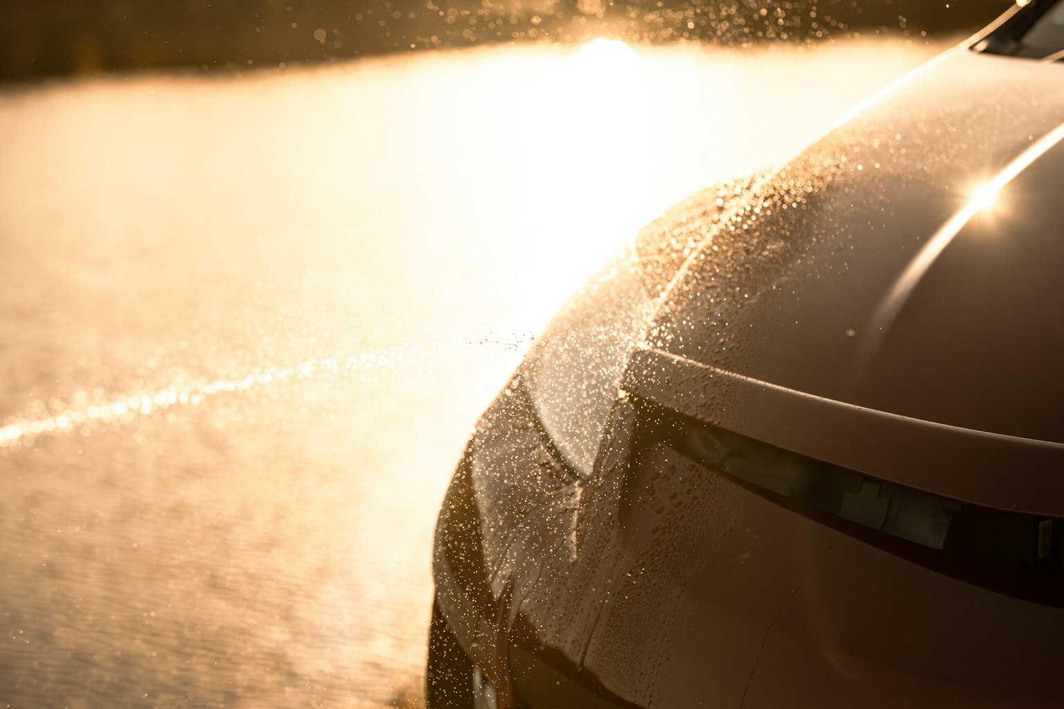 Avant de voiture avec éclaboussures d'eau illuminé par le coucher de soleil