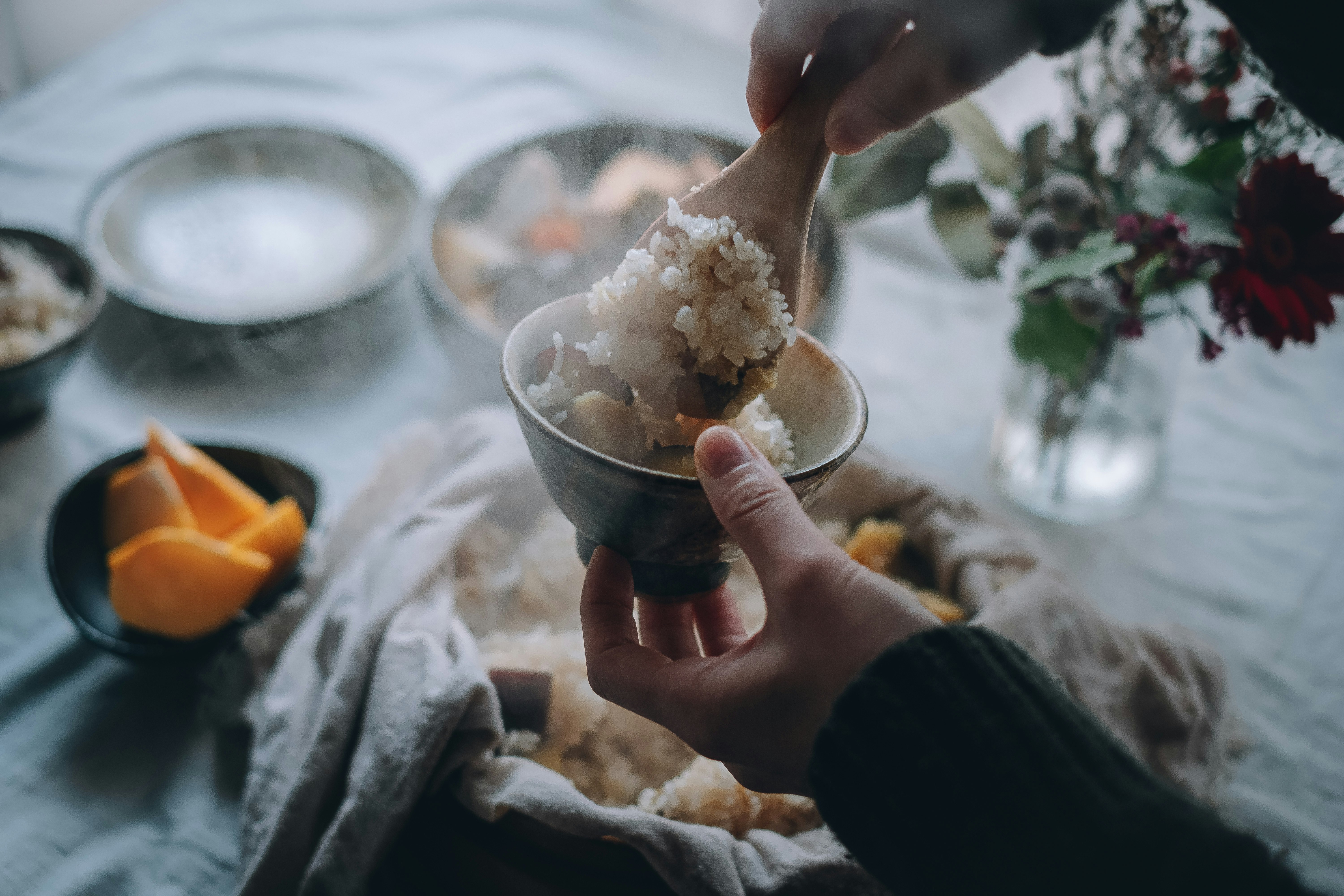 手にお皿を持つ人物がご飯を盛り付けているシーン 花や果物が背景にある