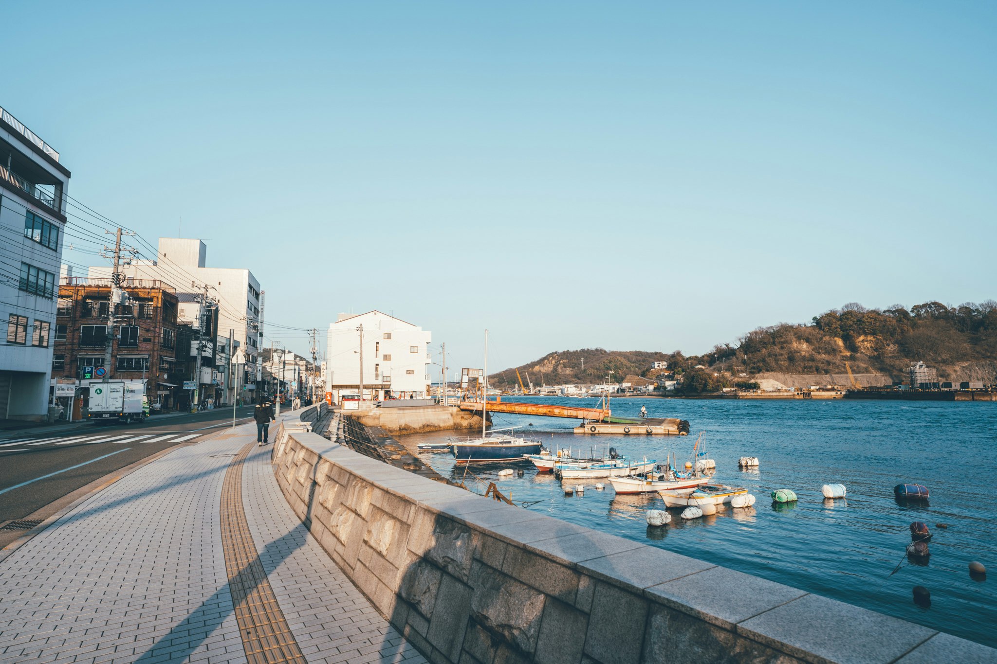 海沿いの遊歩道と係留された小型ボートの並ぶ港の景色