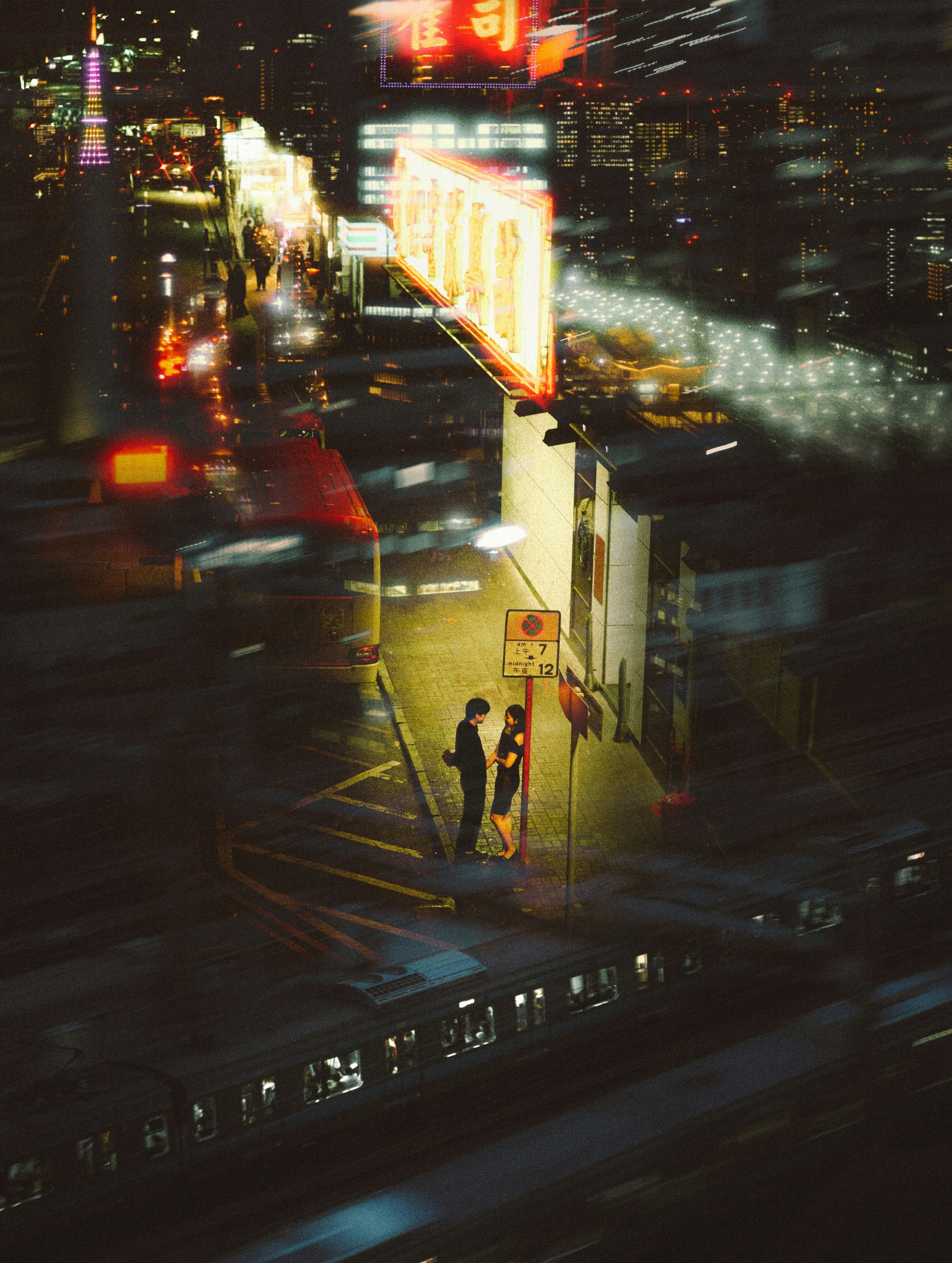 夜の高層ビル街を走る車とネオンの光がにじむ路地の風景