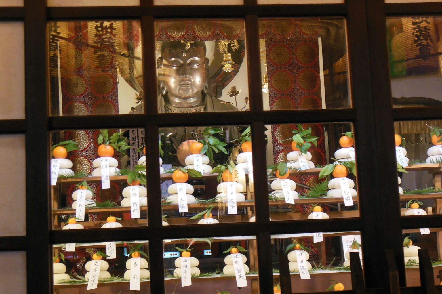 View through a window showcasing a Buddha statue and decorative citrus fruits