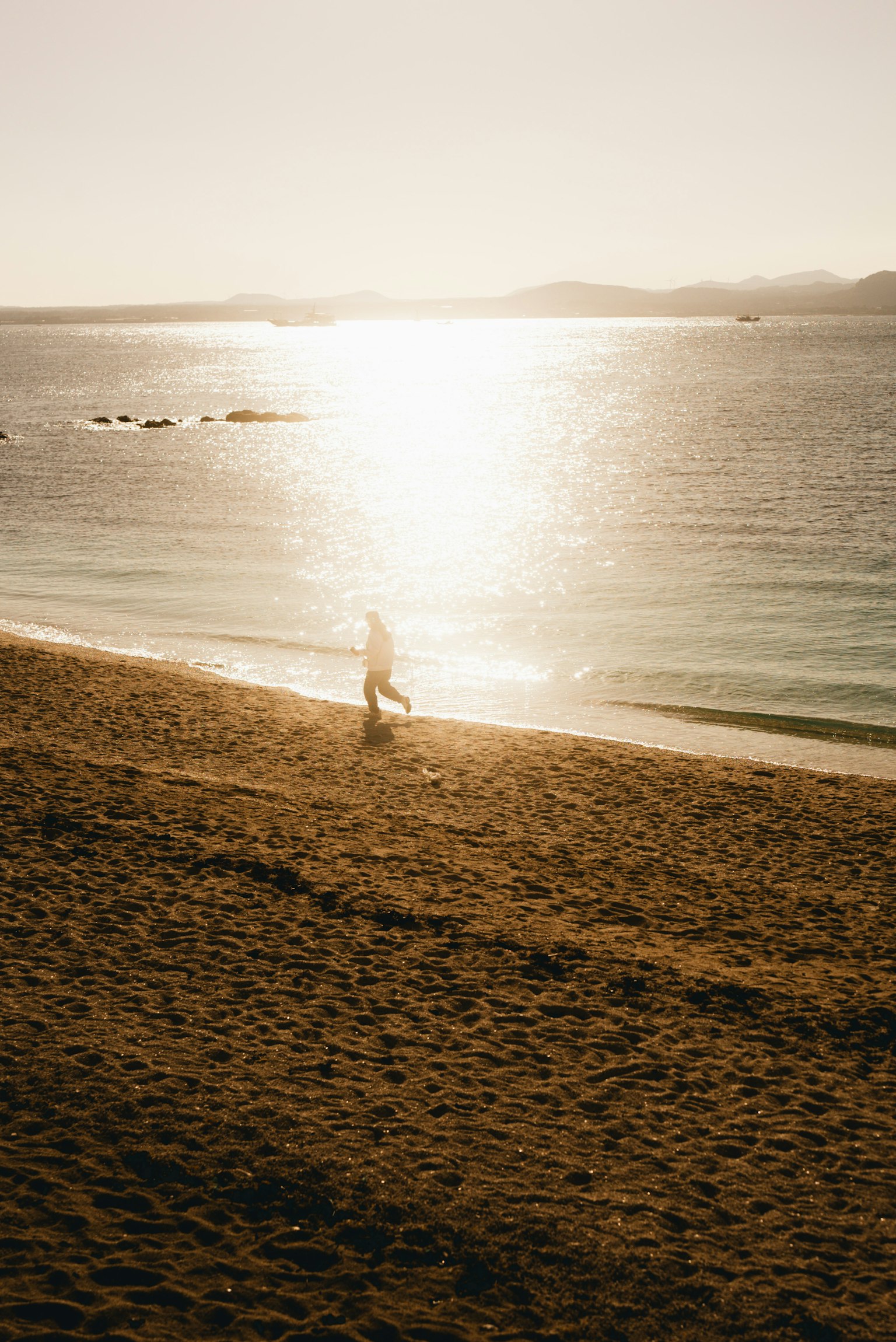 海辺で歩く人のシルエットと輝く水面