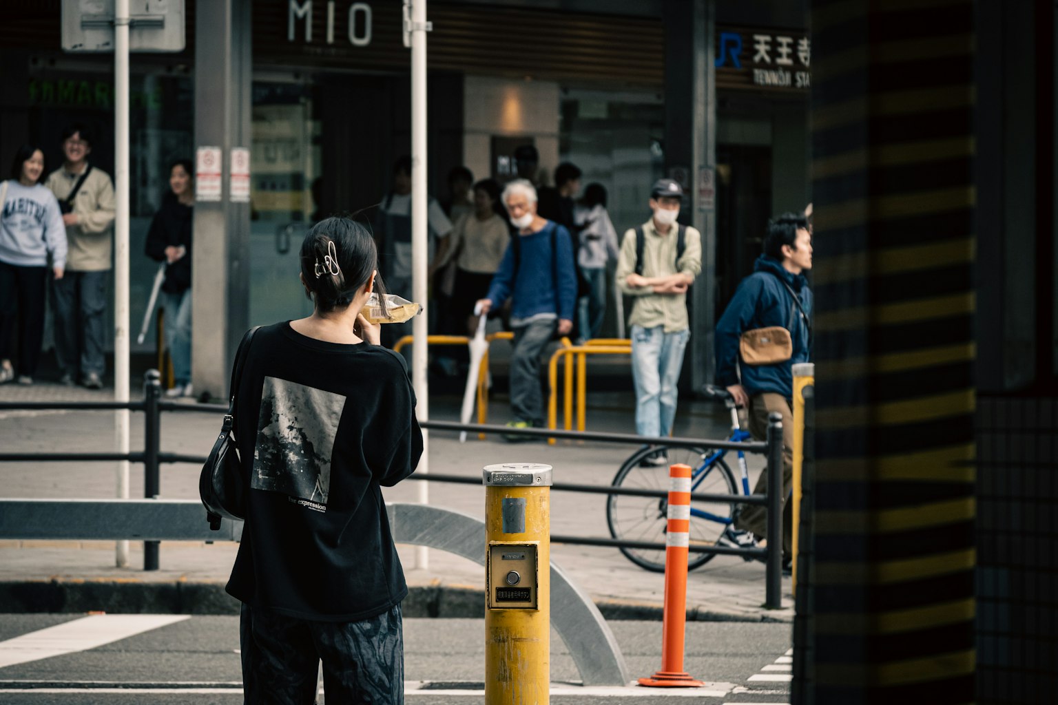 人々が行き交う都市の風景で、背を向けた女性が立っている