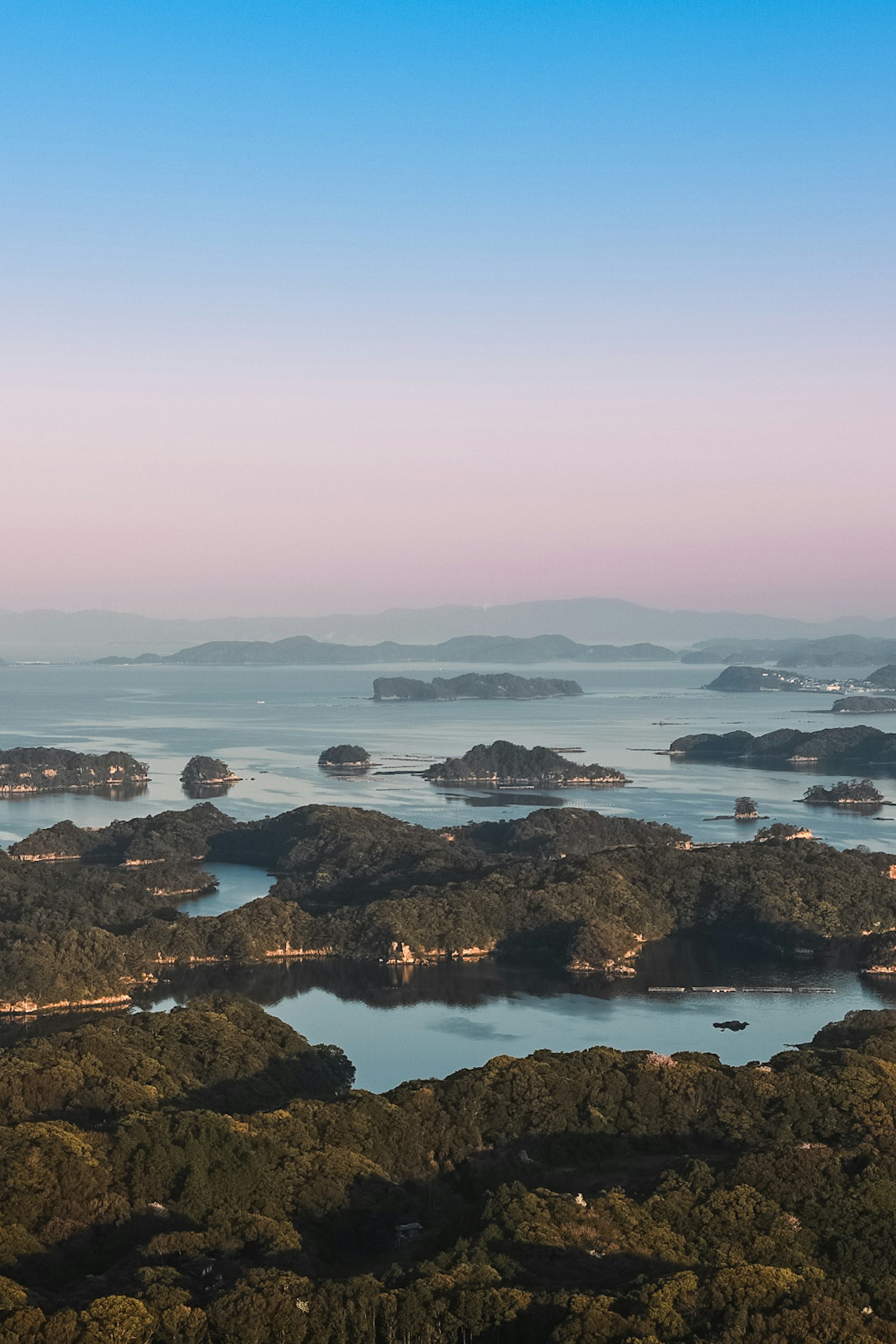 ทิวทัศน์ที่สวยงามของเกาะเขียวชอุ่มที่ล้อมรอบด้วยน้ำใต้ท้องฟ้าสีฟ้าและพื้นหลังสีชมพูอ่อน