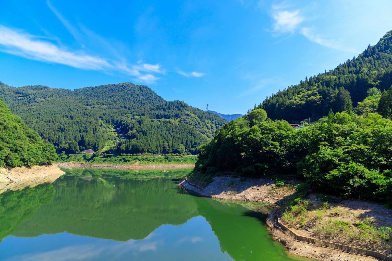 Lago sereno que refleja el cielo azul y las montañas verdes