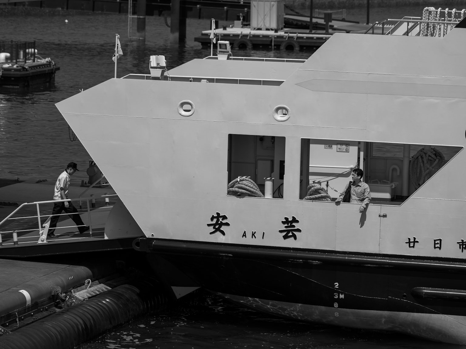 ผู้คนขึ้นเรือข้ามฟากที่มีพื้นหลังเป็นท่าเรือขาวดำ