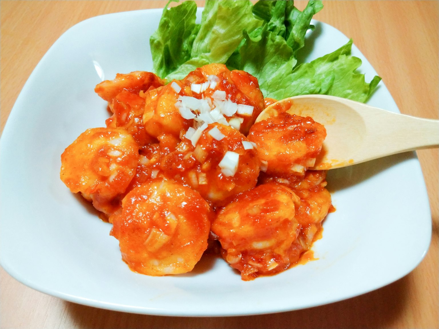 Plate of shrimp in red sauce garnished with chopped onions and lettuce