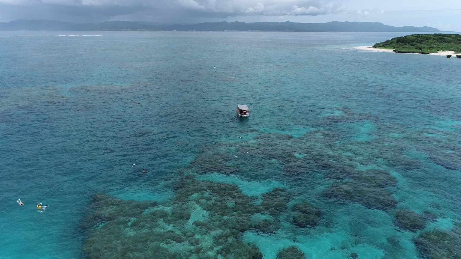一艘船漂浮在碧绿的海面上，附近有游泳的人